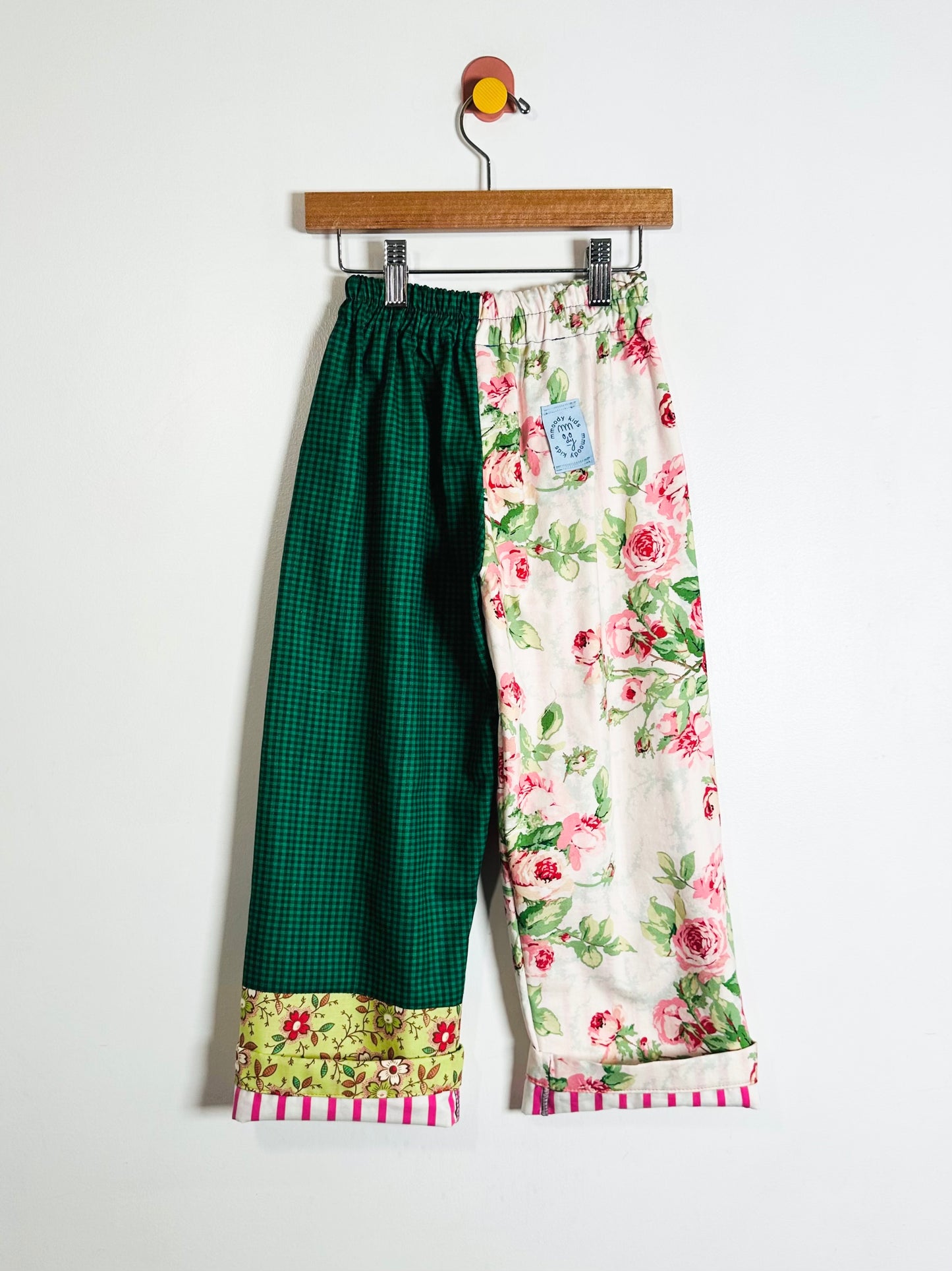 Pair of green and floral-patterned pants on a hanger against a white background