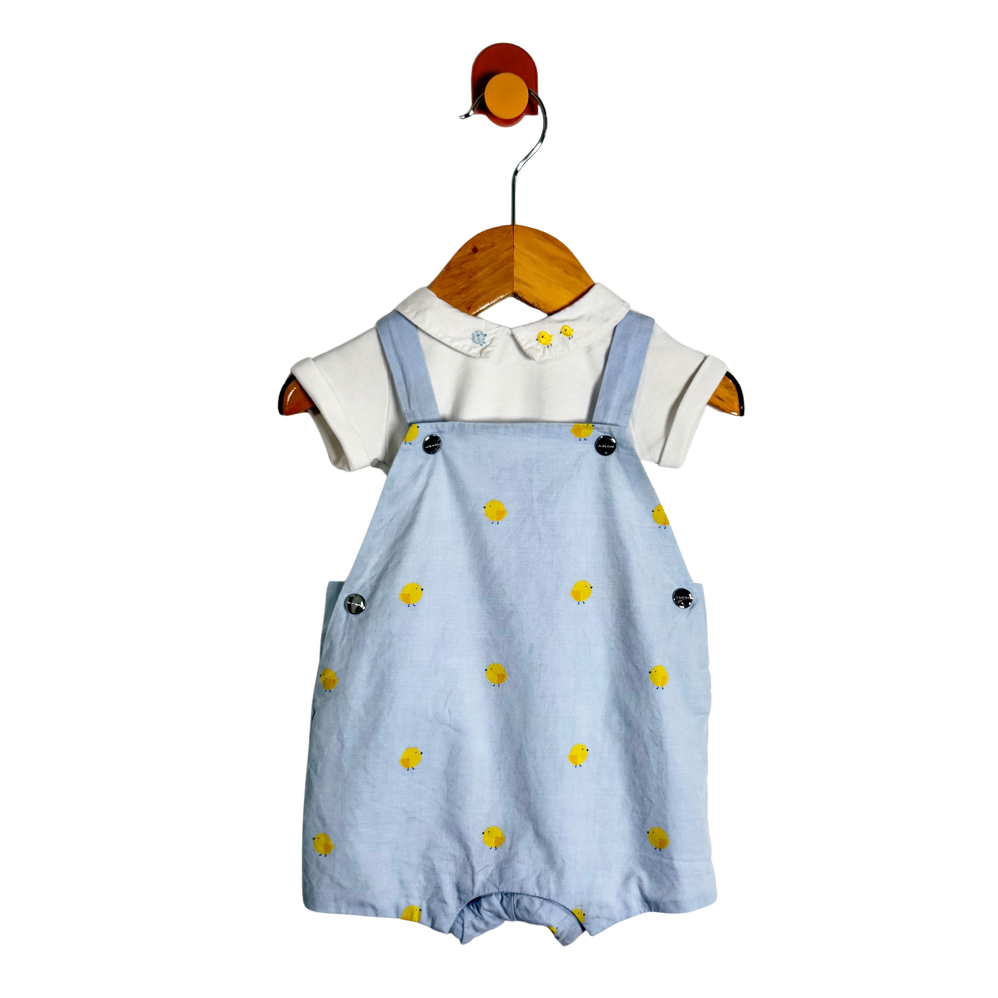 A baby romper set hanging on a wooden hanger against a white background. The set includes light blue denim-style overall shorts with yellow chick prints and a white short-sleeve top with a decorative collar.