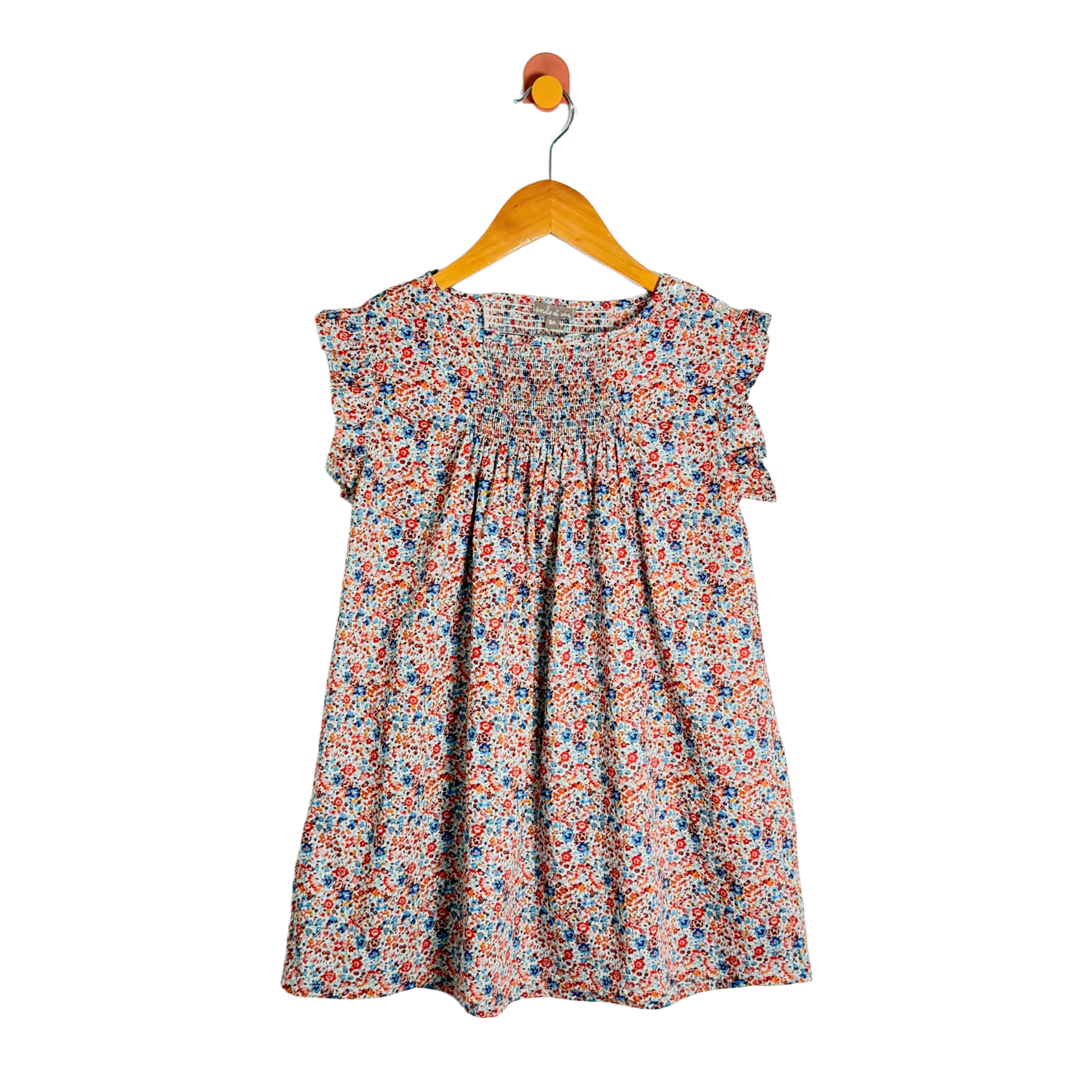 A children's short-sleeve dress with a dense multicolor floral print, hanging on a wooden hanger against a plain white background.
