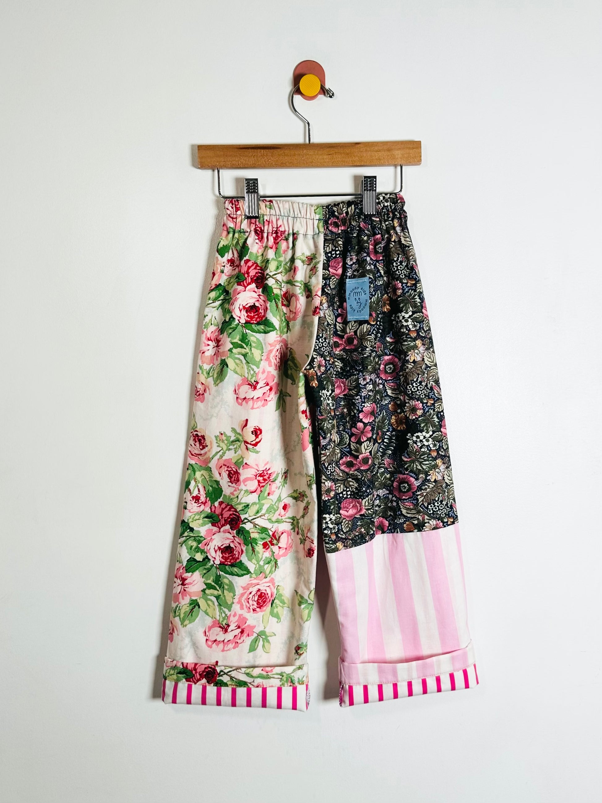 Colorful floral and striped pants on a hanger against a white background