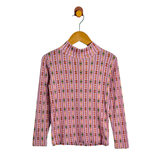A pink long-sleeve mock neck top with a vertical multicolor geometric pattern, hanging on a wooden hanger against a white background.