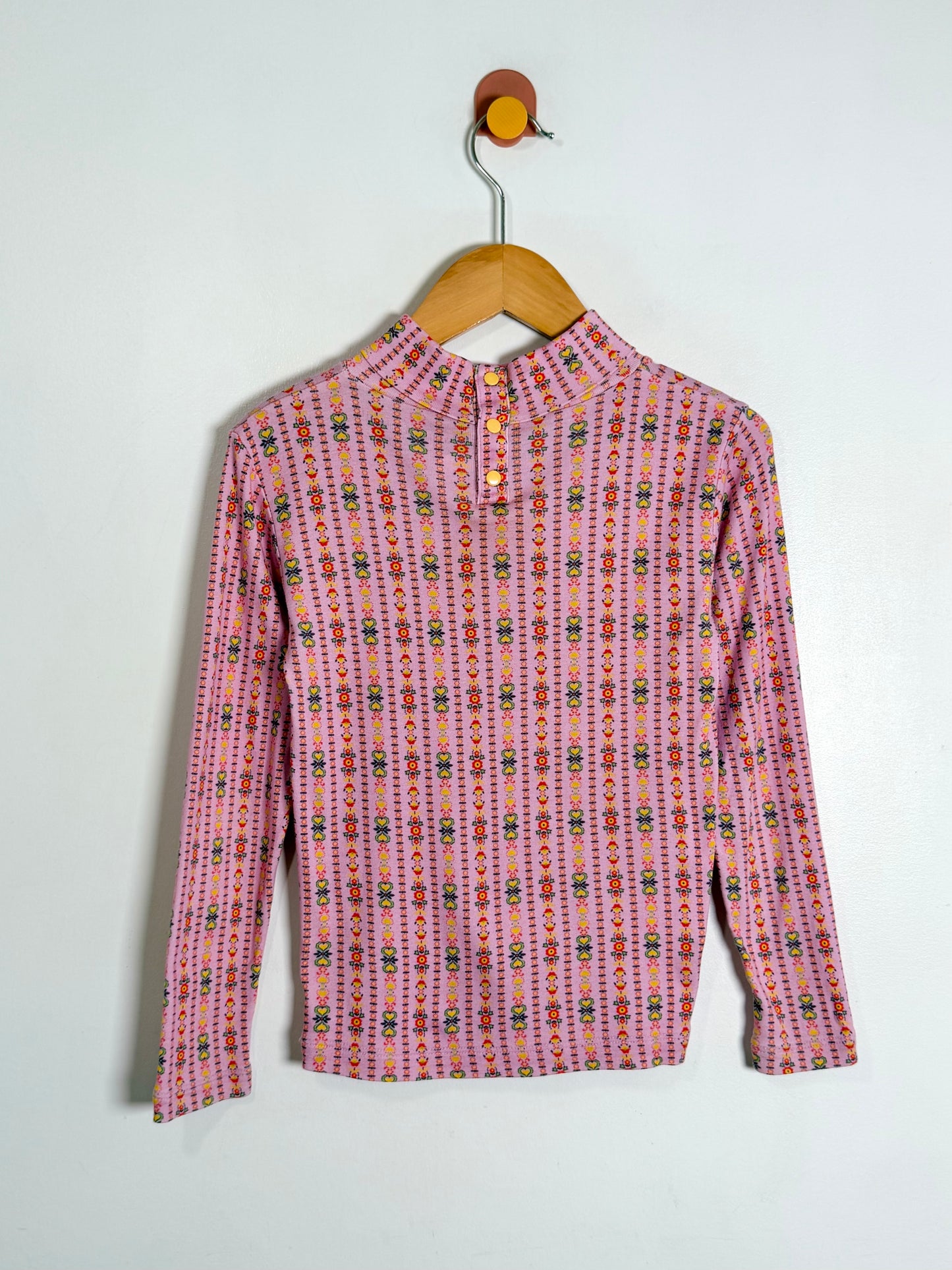 A pink long-sleeve button-up shirt with a colorful geometric pattern, hanging on a wooden hanger against a plain white wall.