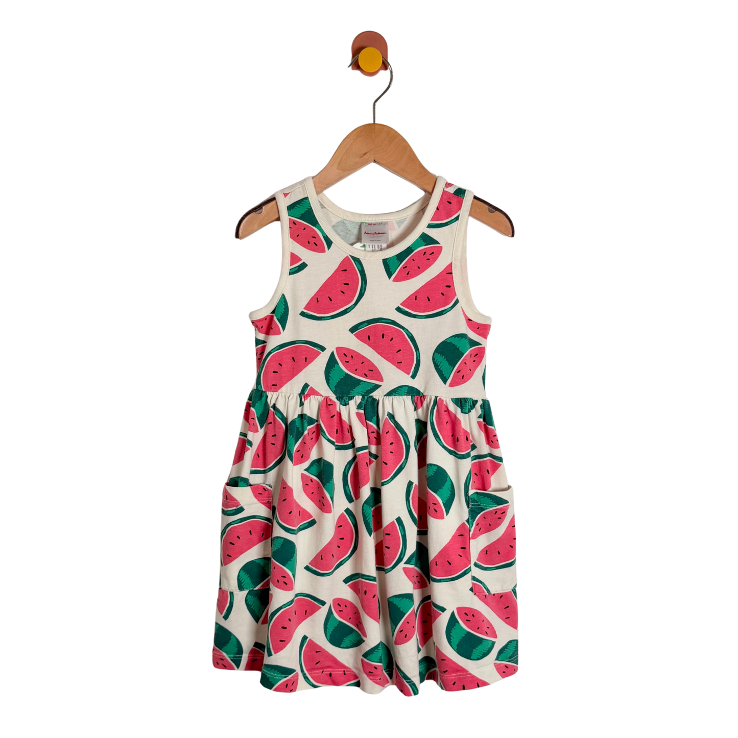 A sleeveless children's dress with an all-over watermelon print, hanging on a wooden hanger against a plain white background.