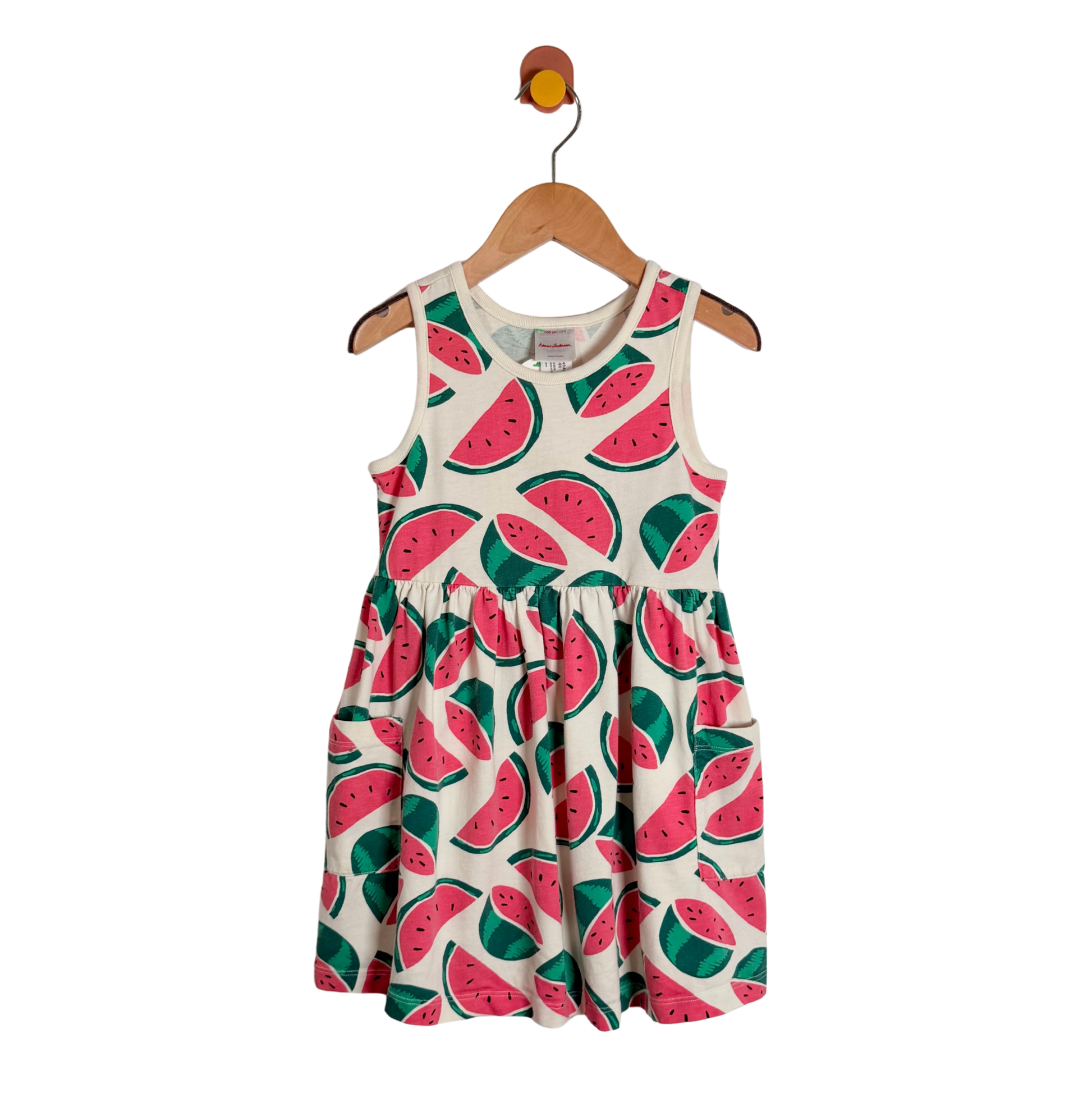 A sleeveless children's dress with an all-over watermelon print, hanging on a wooden hanger against a plain white background.