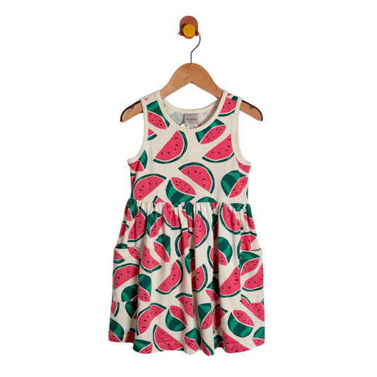 A sleeveless children's dress with an all-over watermelon print, hanging on a wooden hanger against a plain white background.