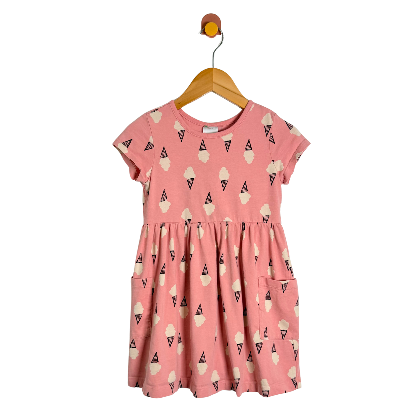 A pink short-sleeve children's dress with an all-over ice cream cone print, hanging on a wooden hanger against a plain white background.