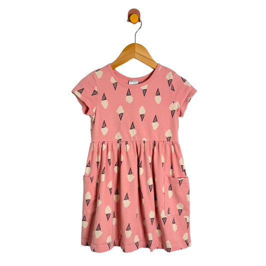 A pink short-sleeve children's dress with an all-over ice cream cone print, hanging on a wooden hanger against a plain white background.