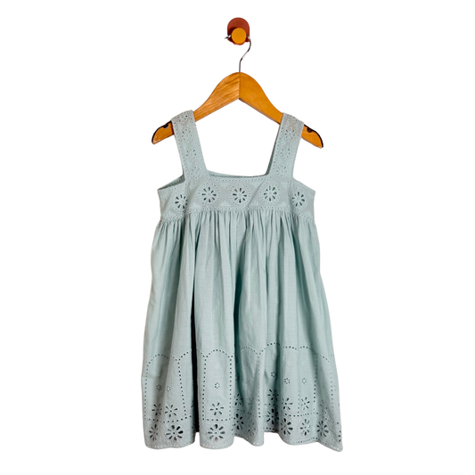 A light sage green eyelet cotton dress for kids, hanging on a wooden hanger against a solid white background.