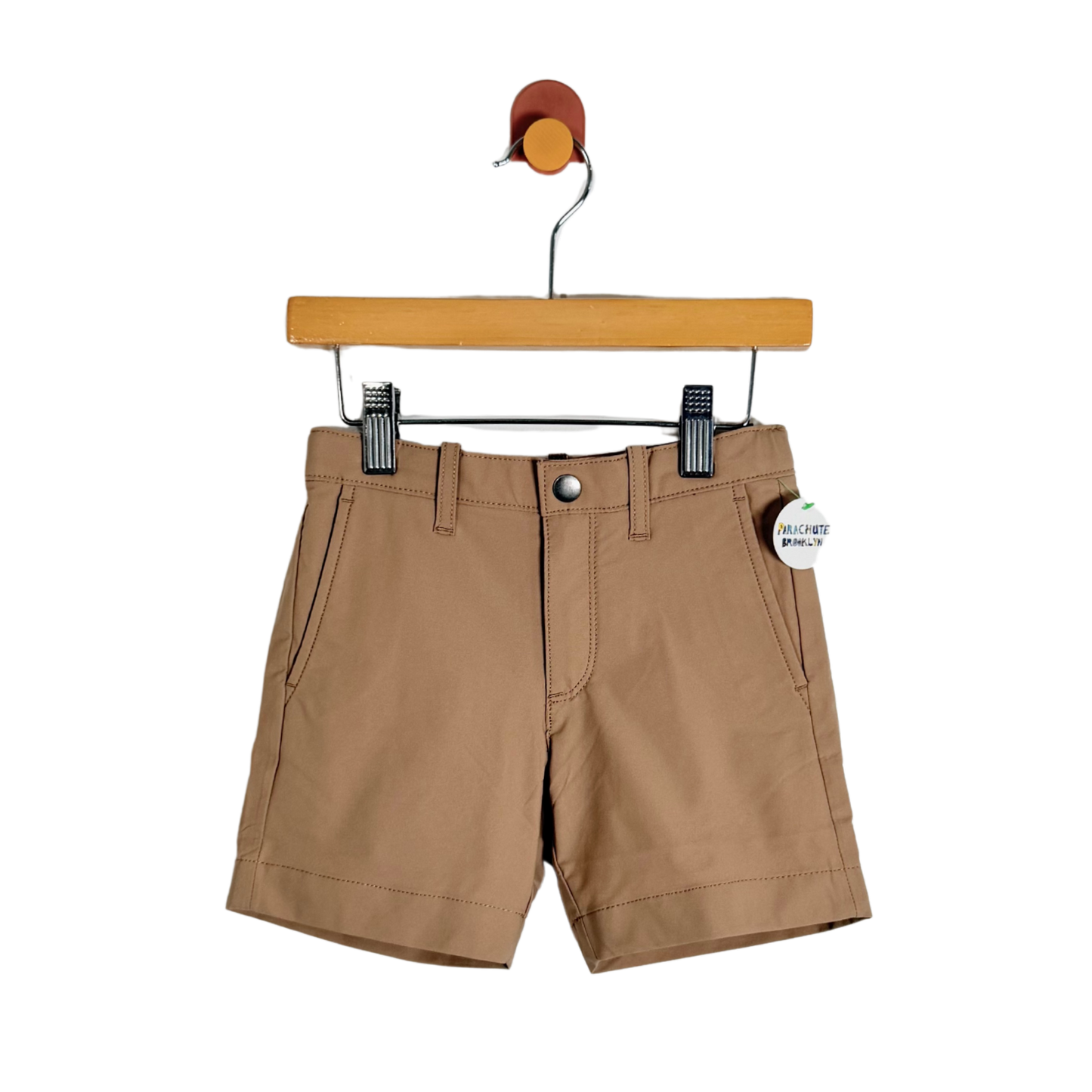 A pair of tan chino shorts hanging from a wooden hanger with black clips against a plain white background.