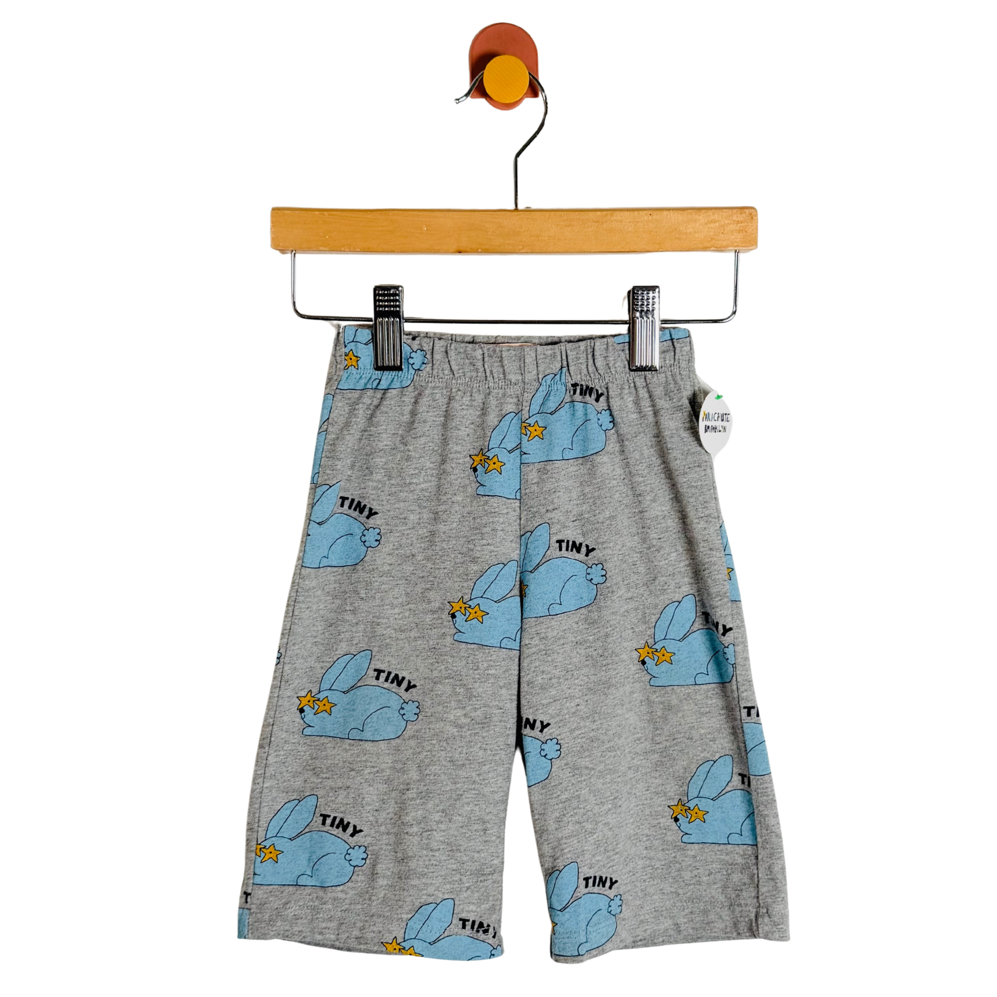 Gray heathered shorts with a blue bunny print and 'TINY' text, hanging on a wooden hanger against a white background.