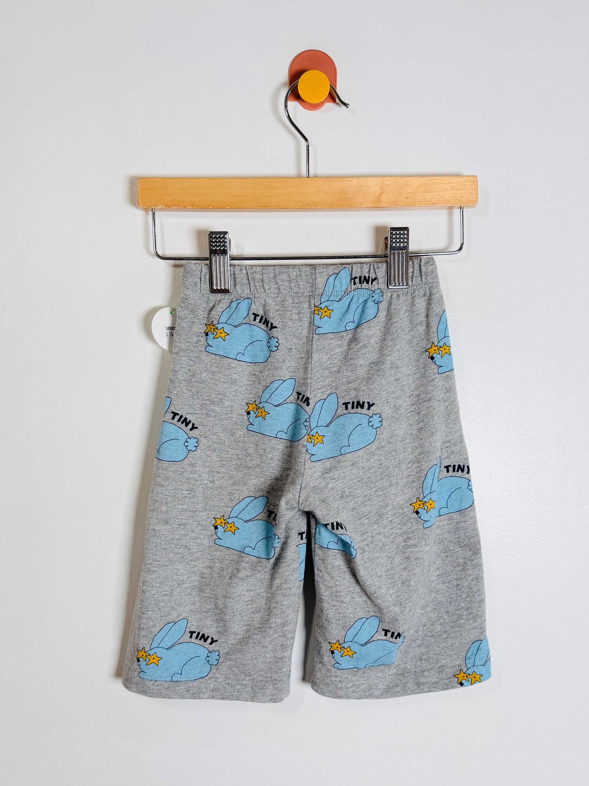 Gray heathered children's shorts with a light blue bunny print and small yellow accents, hanging from a wooden hanger against a plain light background.