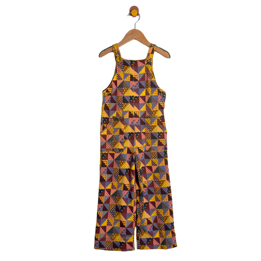 A sleeveless wide-leg jumpsuit with a colorful geometric patchwork print, hanging on a wooden hanger against a plain white background.