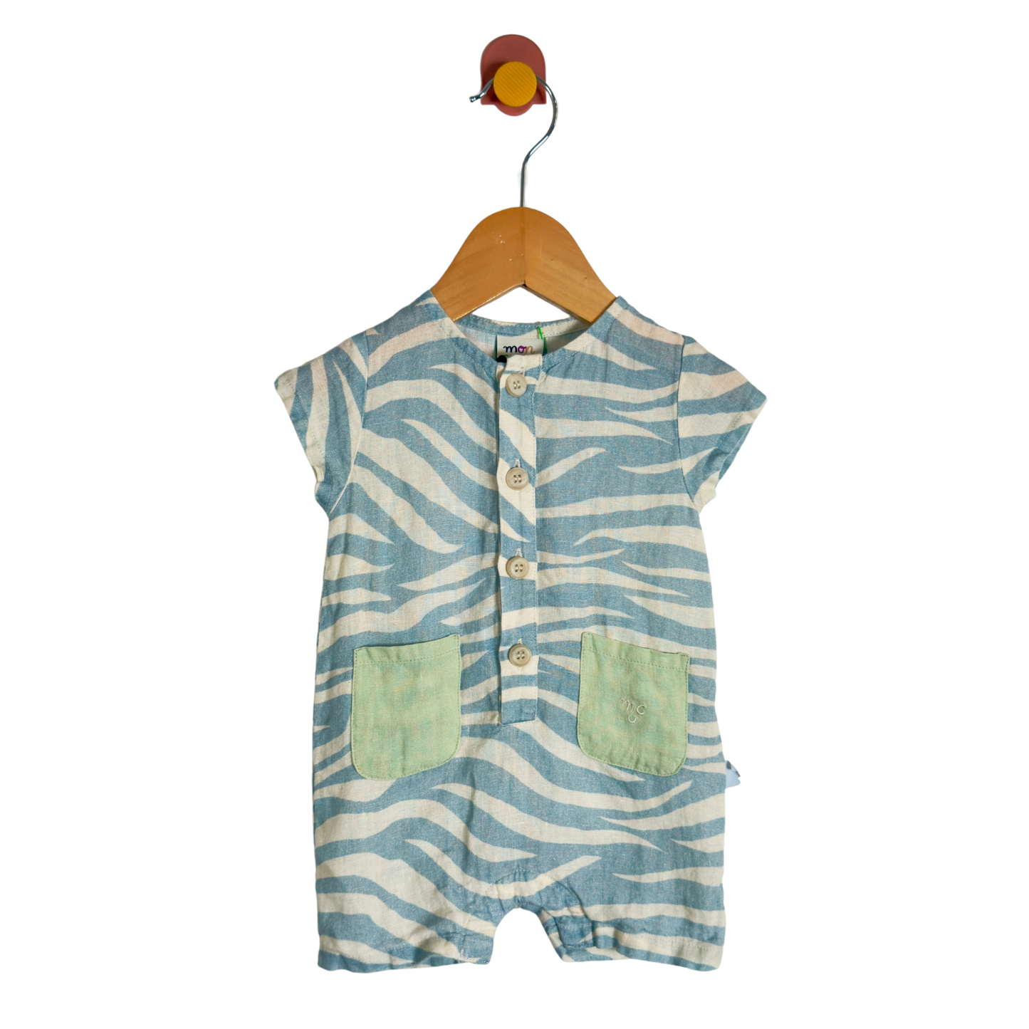 A baby short-sleeve romper with a blue and white zebra stripe pattern, featuring two light green front pockets and a button-up front, hanging on a wooden hanger against a white background.
