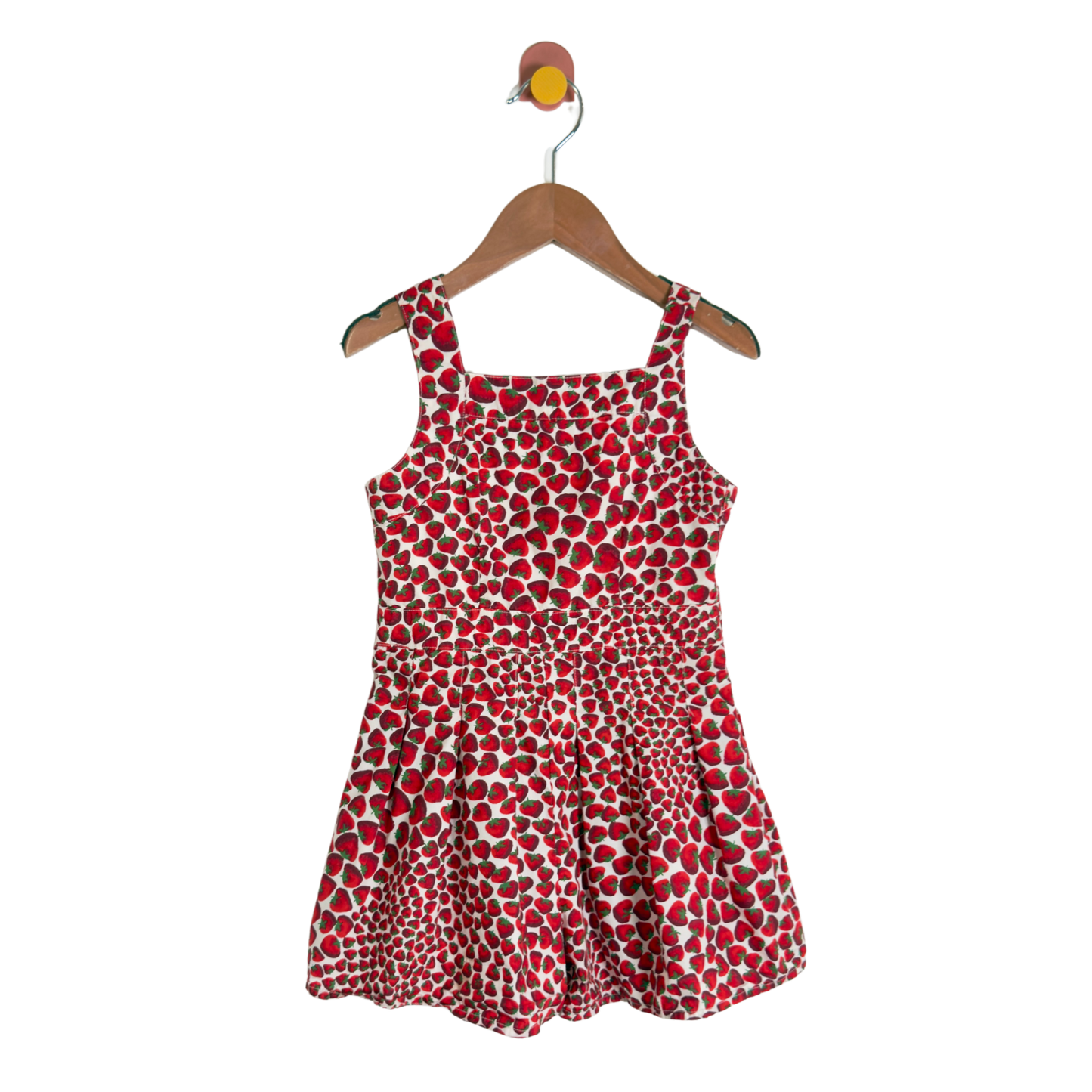 A sleeveless children's dress with a red, white, and black spotted pattern, hanging on a wooden hanger against a plain white background.