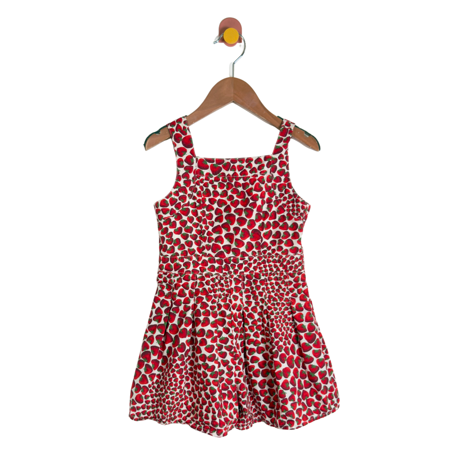 A sleeveless children's dress with a red, white, and black spotted pattern, hanging on a wooden hanger against a plain white background.