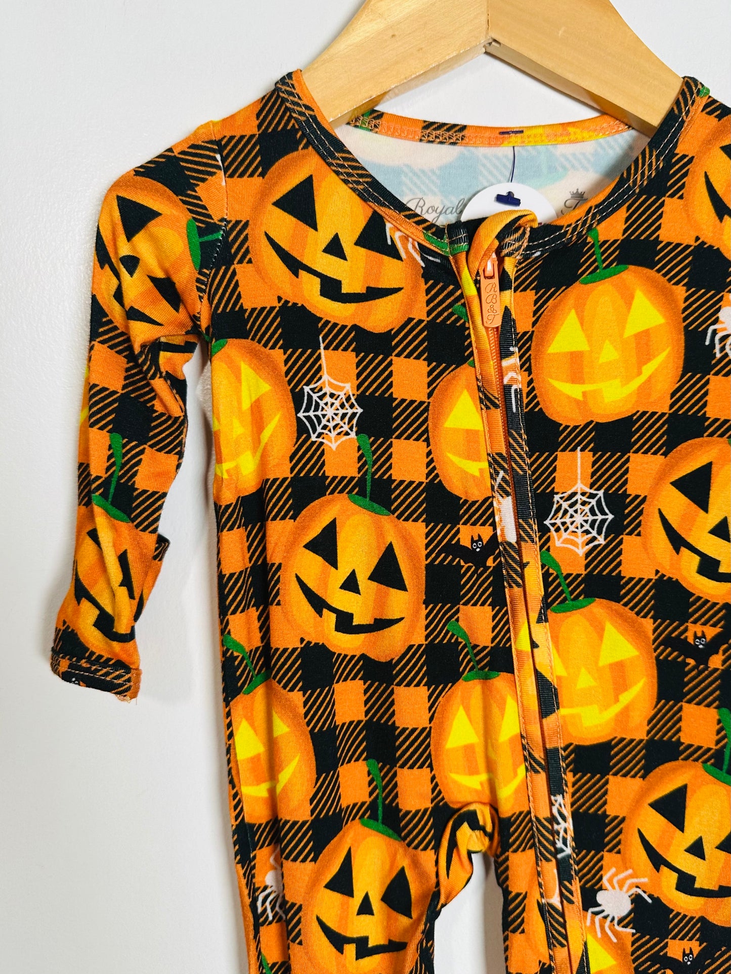 Halloween-themed onesie with pumpkins on a hanger against a white background