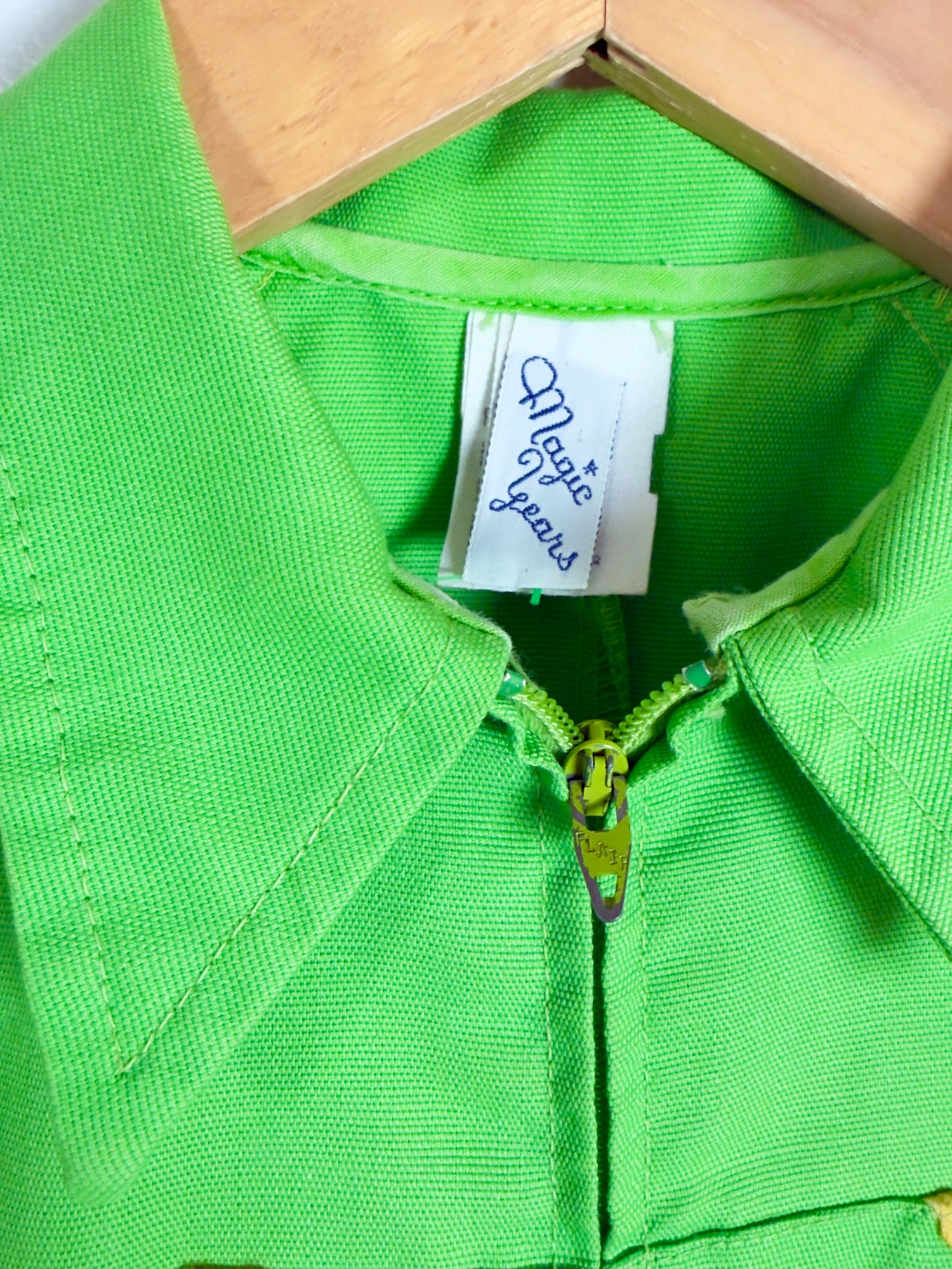 Close-up of a bright lime green zippered garment on a wooden hanger, showing a white neck label that reads 'Magic yarns'.