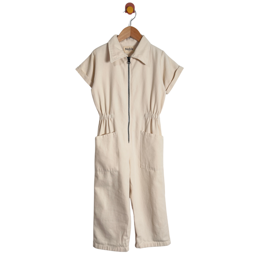 A cream-colored short-sleeve jumpsuit with a half-zip front, collar, and front patch pockets, hanging on a wooden hanger against a white background.