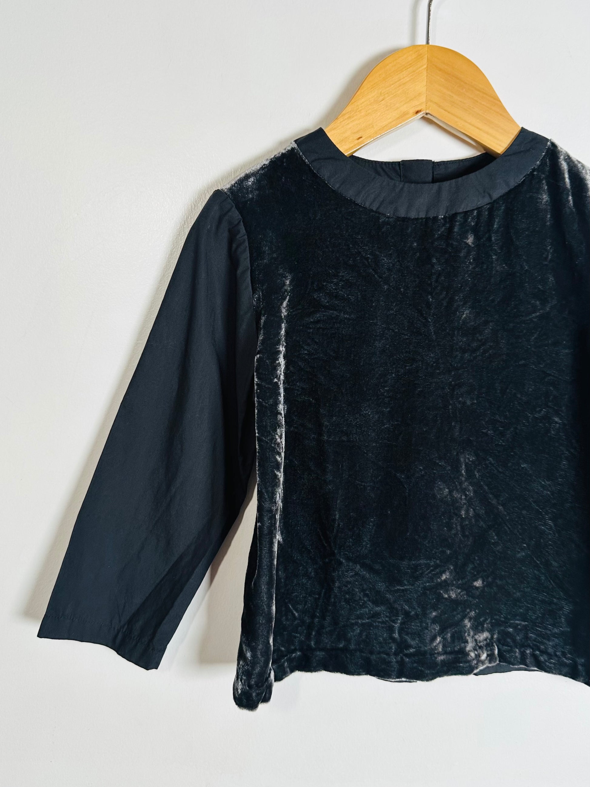 Black textured long-sleeve top on a wooden hanger against a white background