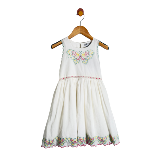 A sleeveless white children's dress with a colorful butterfly embroidery on the chest and a floral embroidered hem, hanging on a wooden hanger against a white background.