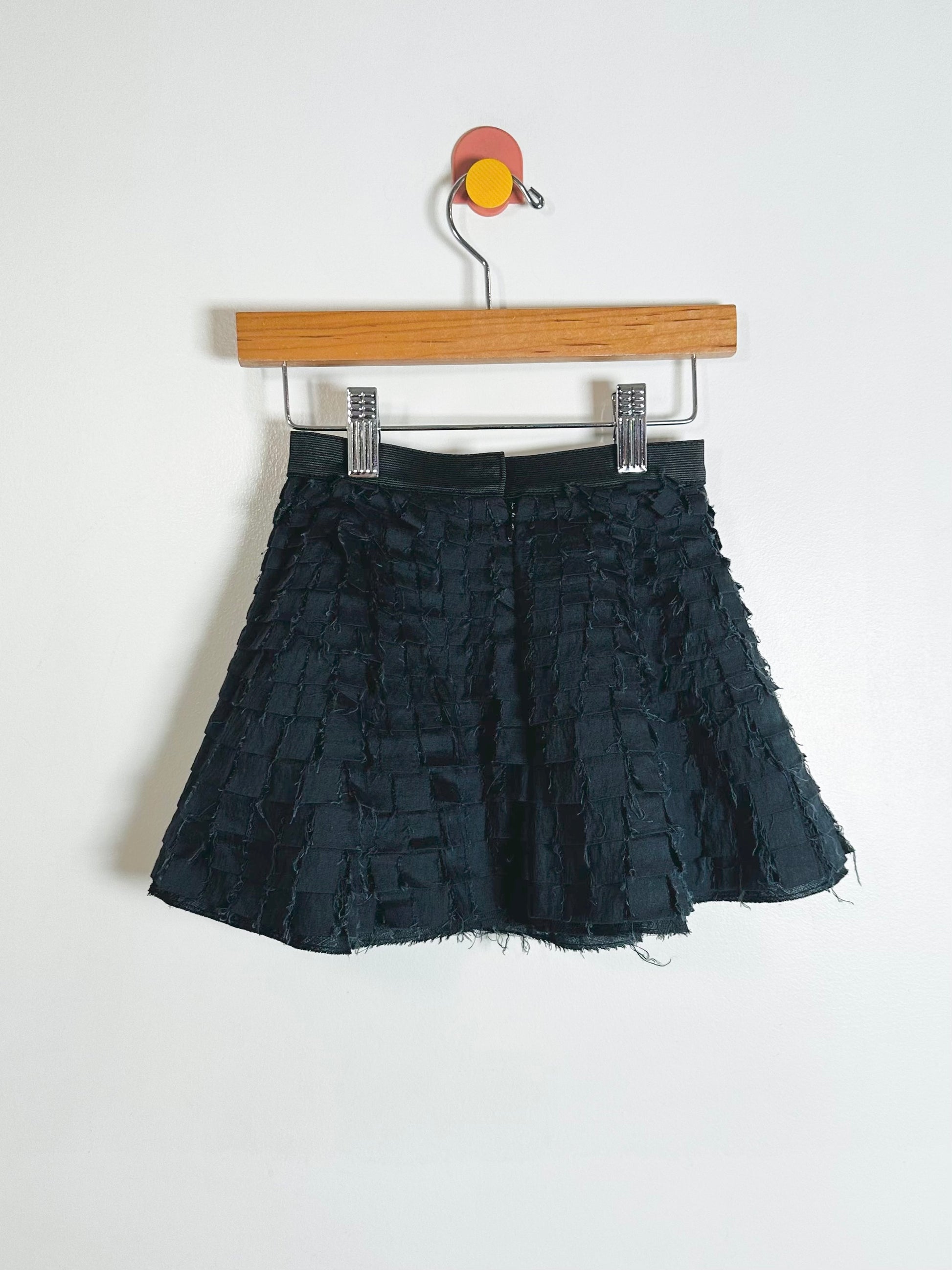 Black textured skirt on a wooden hanger against a white background