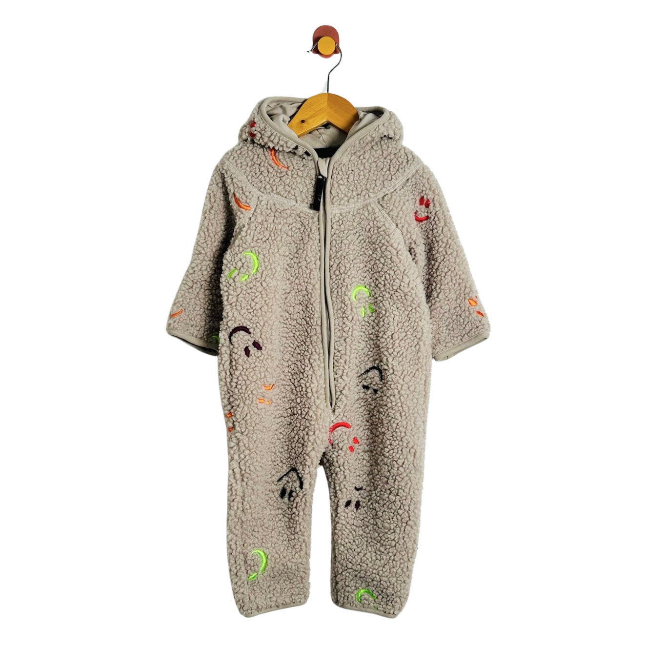 A baby hooded one-piece fleece jumpsuit in a warm taupe-beige color, decorated with colorful cartoon face prints, hanging on a wooden hanger against a plain white background.