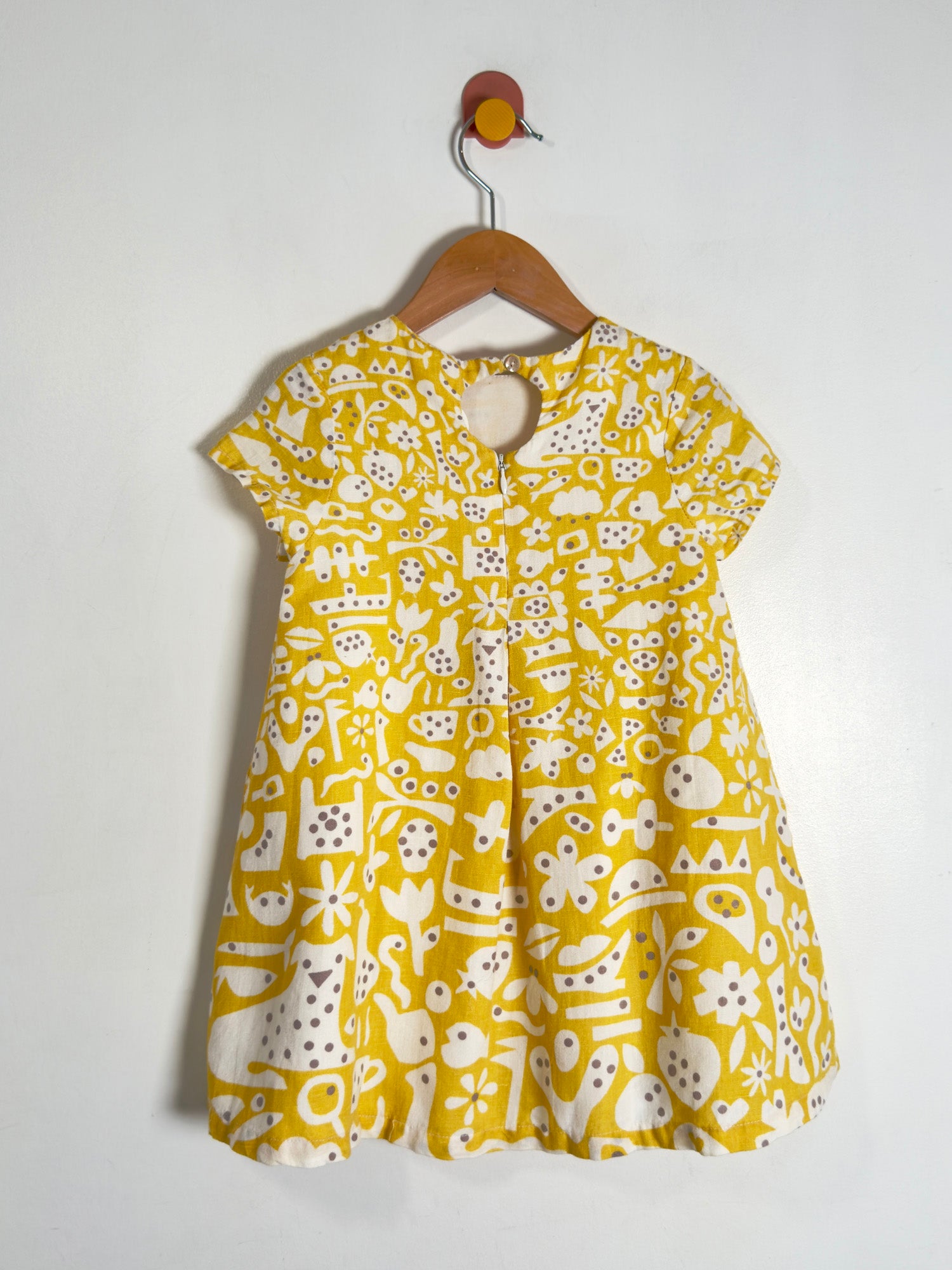 A yellow short-sleeve dress with a white and gray abstract pattern, hanging on a wooden hanger against a plain white wall.
