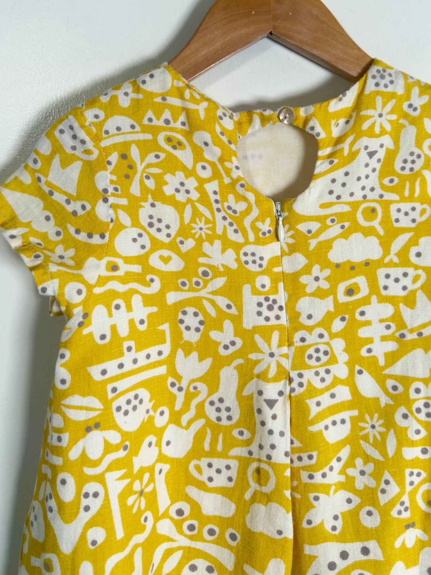 A yellow short-sleeve top with a white abstract pattern, hanging on a wooden hanger against a plain light background.