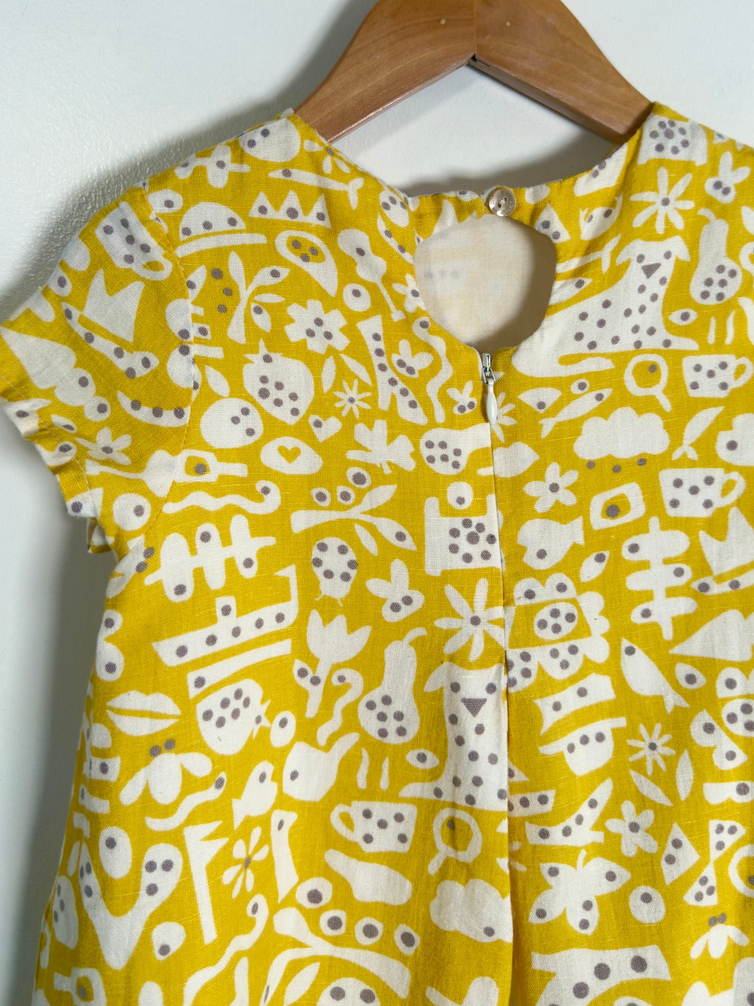 A yellow short-sleeve top with a white abstract pattern, hanging on a wooden hanger against a plain light background.