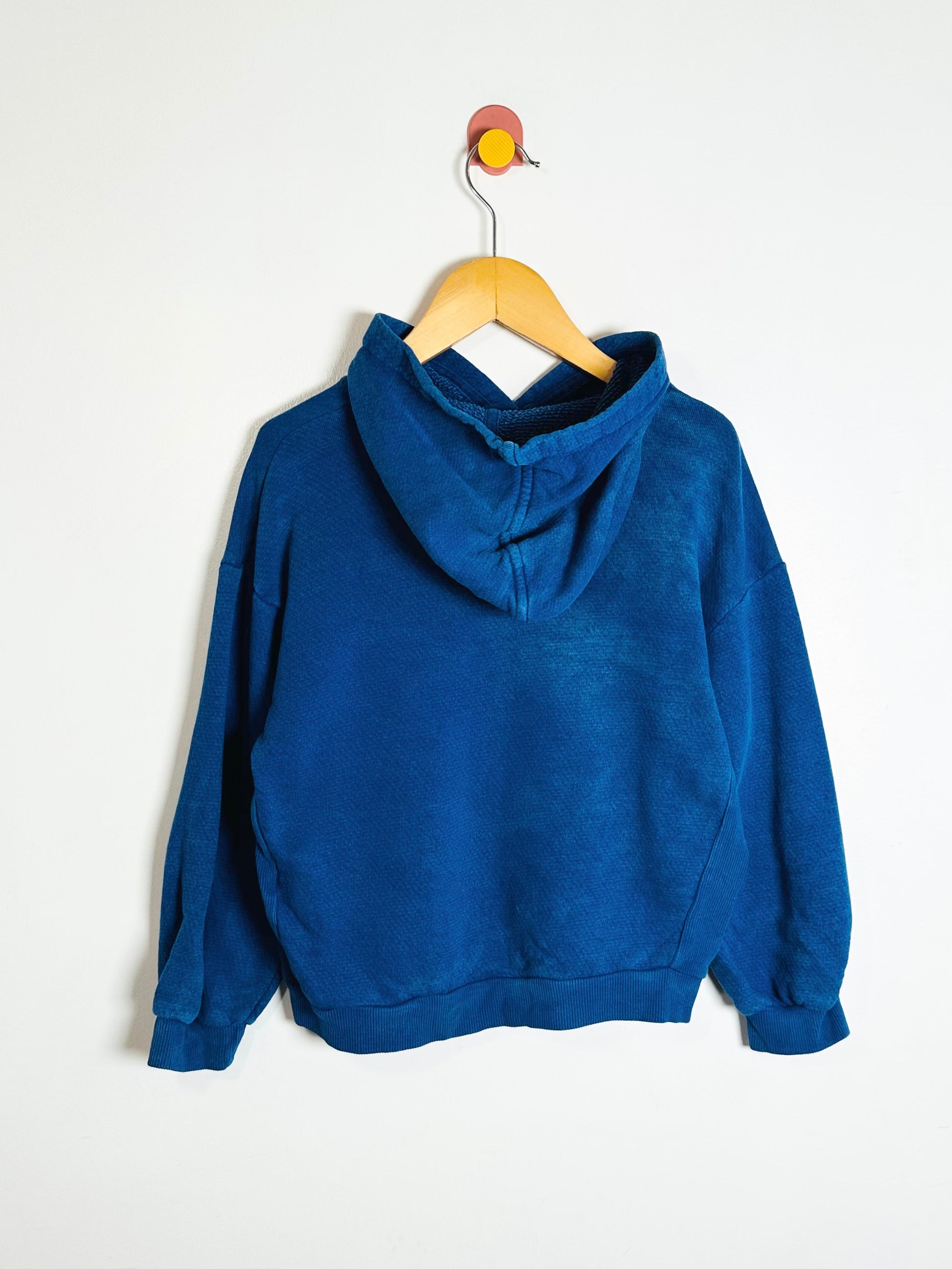 Blue hoodie on a wooden hanger against a white background
