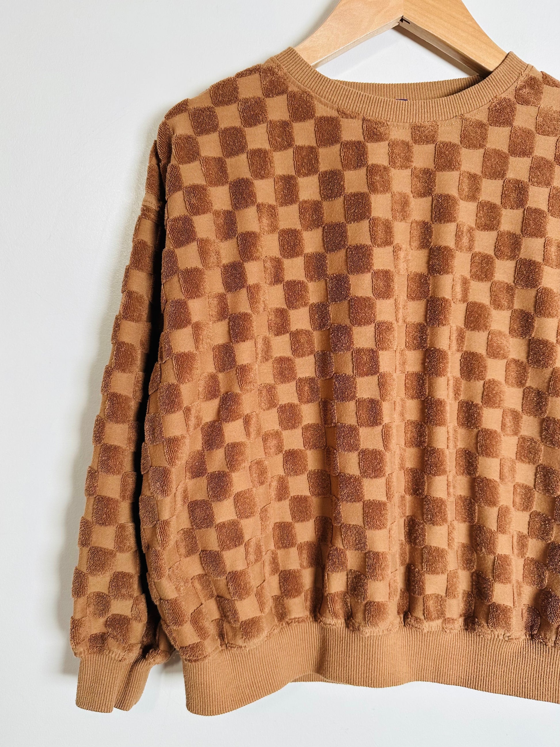 Brown checkered sweater on a hanger against a white background