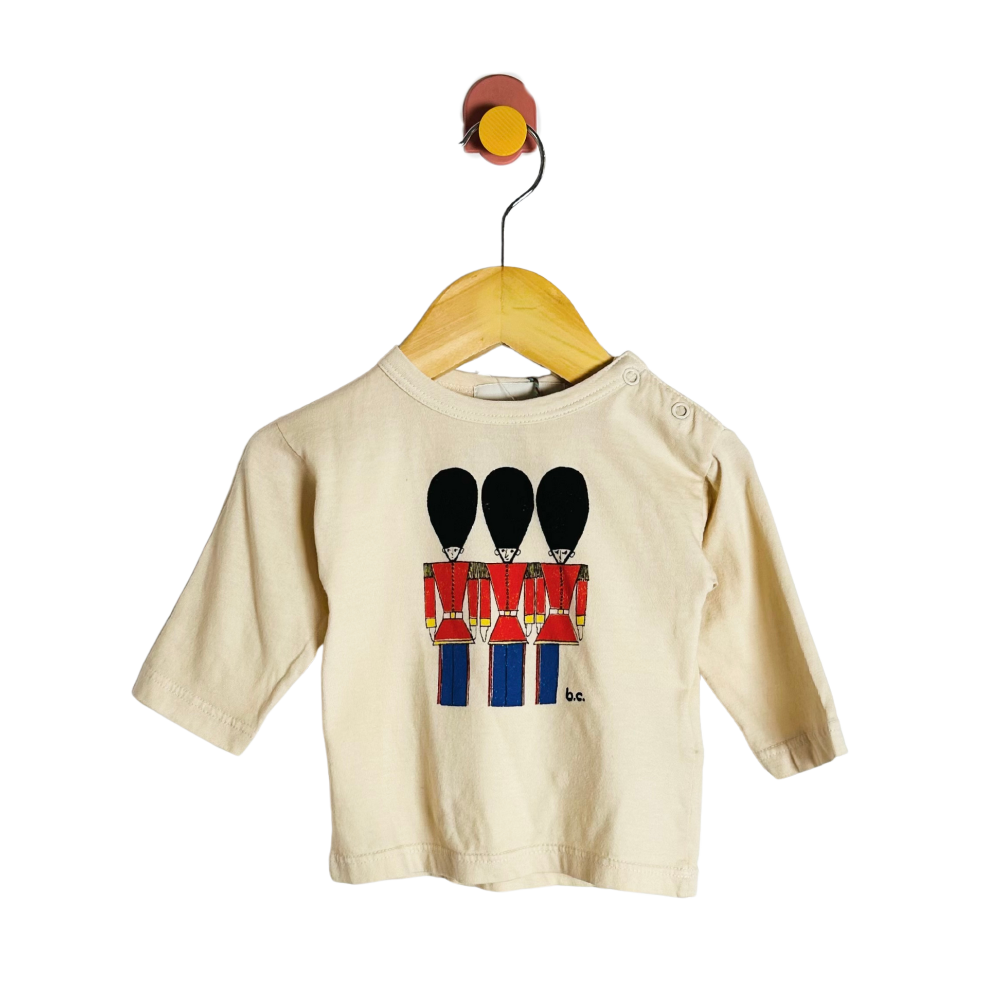 Beige long-sleeve shirt with toy soldier design on a wooden hanger against a white background