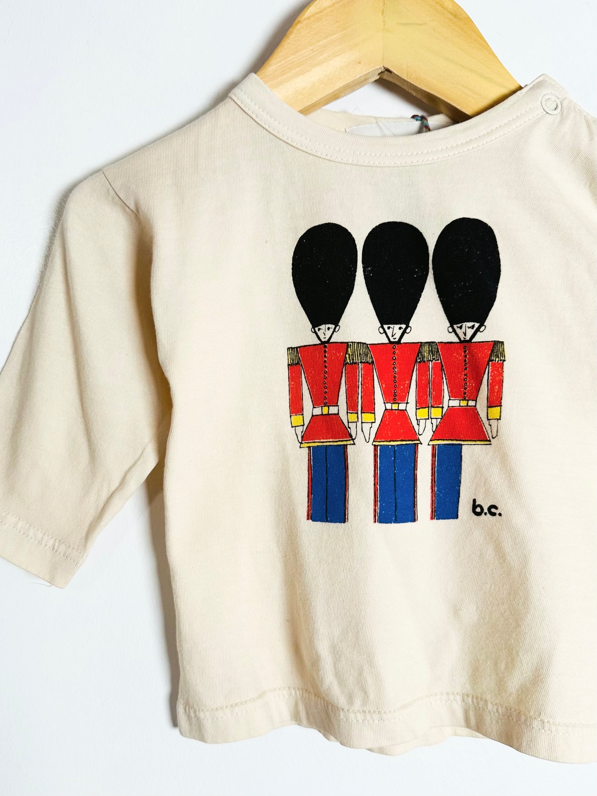 Beige t-shirt with a graphic of three soldiers in red uniforms on a white background