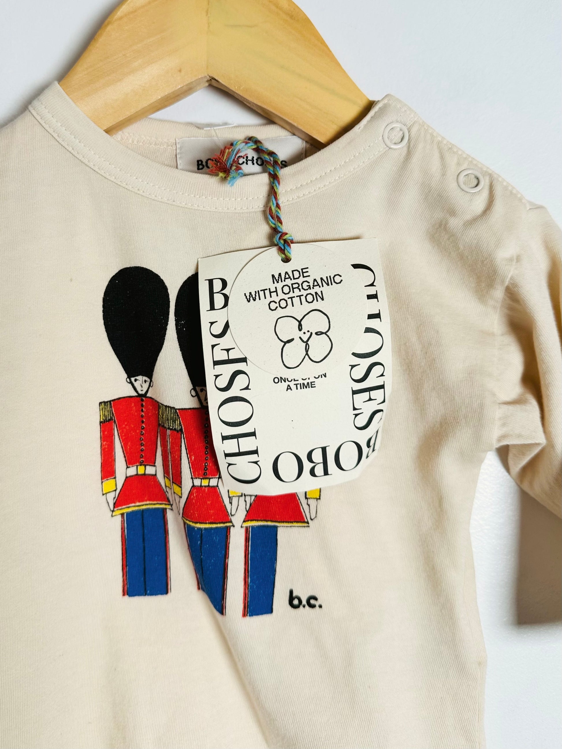 Beige baby onesie with a cartoon guard design and a visible tag on a white background