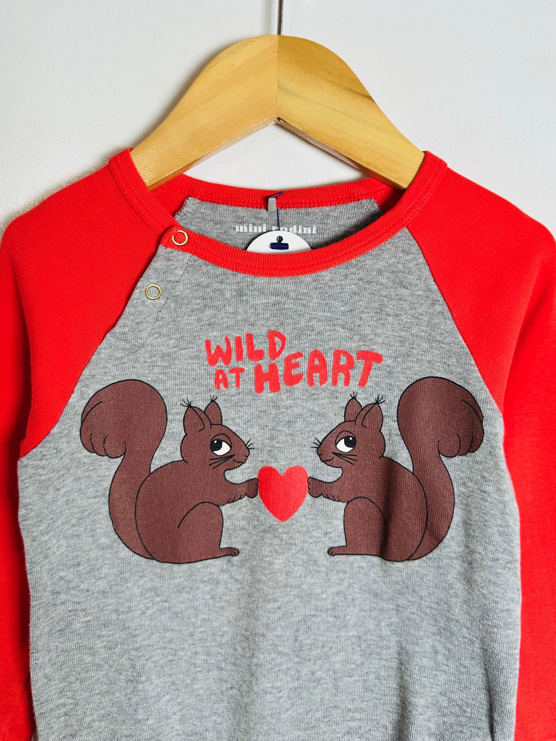 Children's shirt with two squirrels holding a heart and 'Wild at Heart' text on a hanger.
