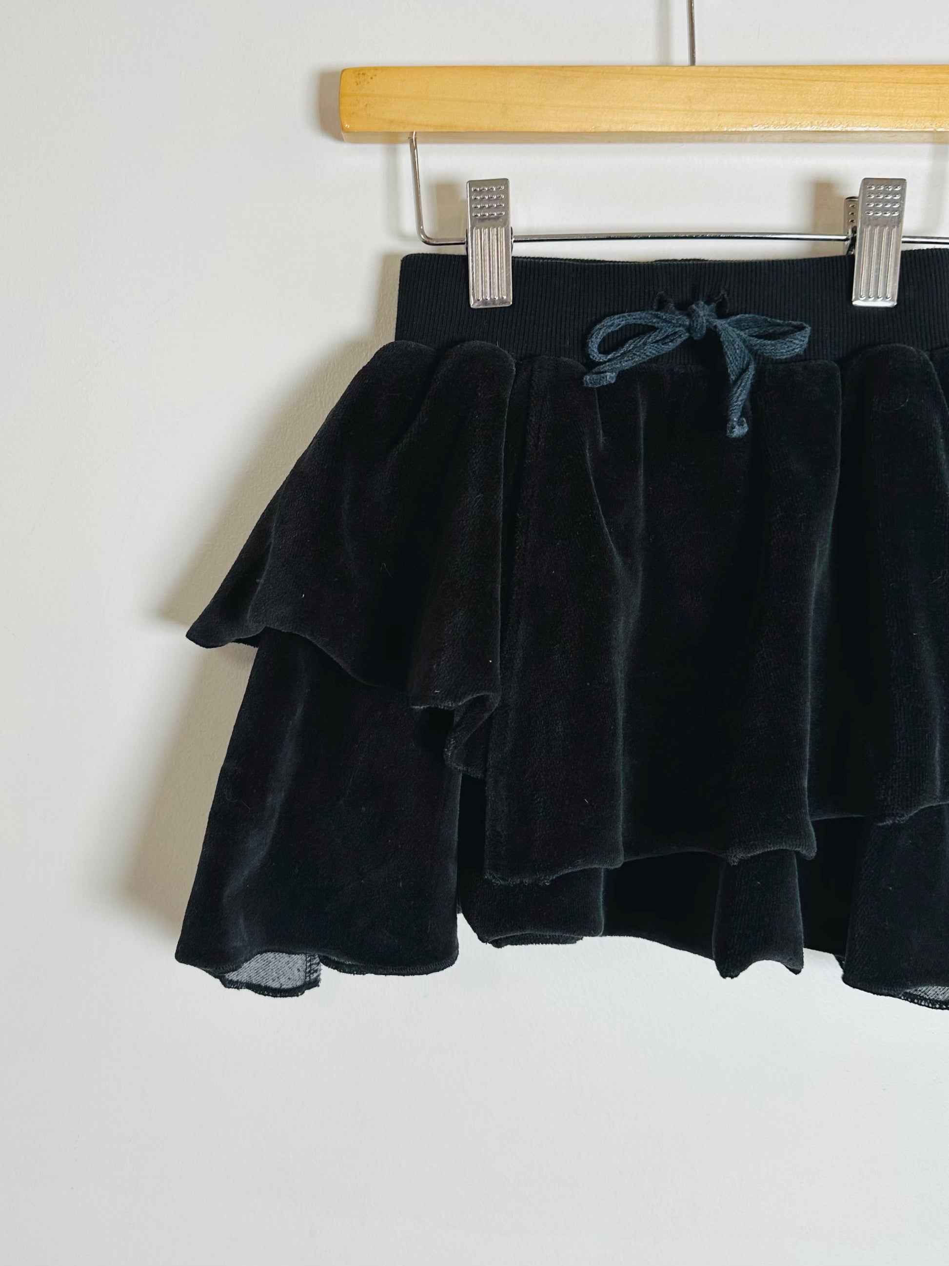 Black velvet skirt on a hanger against a white background