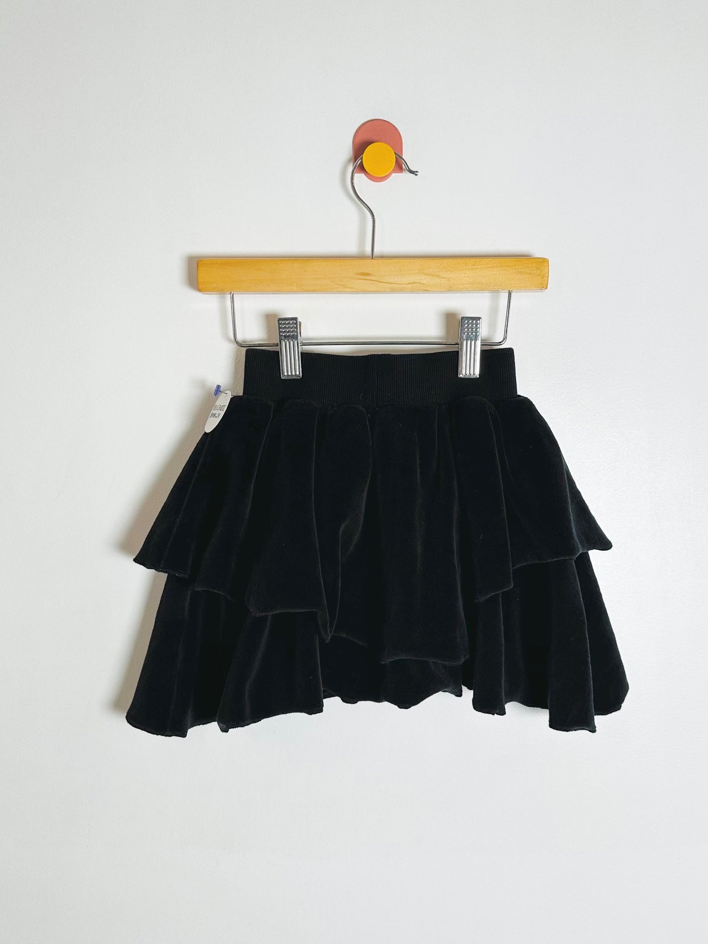 Black tiered skirt on a wooden hanger against a white background