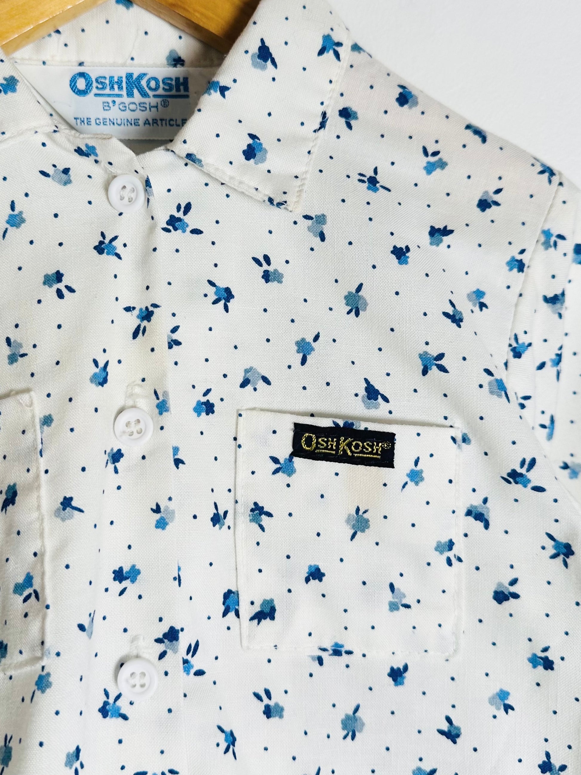 White shirt with blue floral pattern and OshKosh branding on a wooden surface