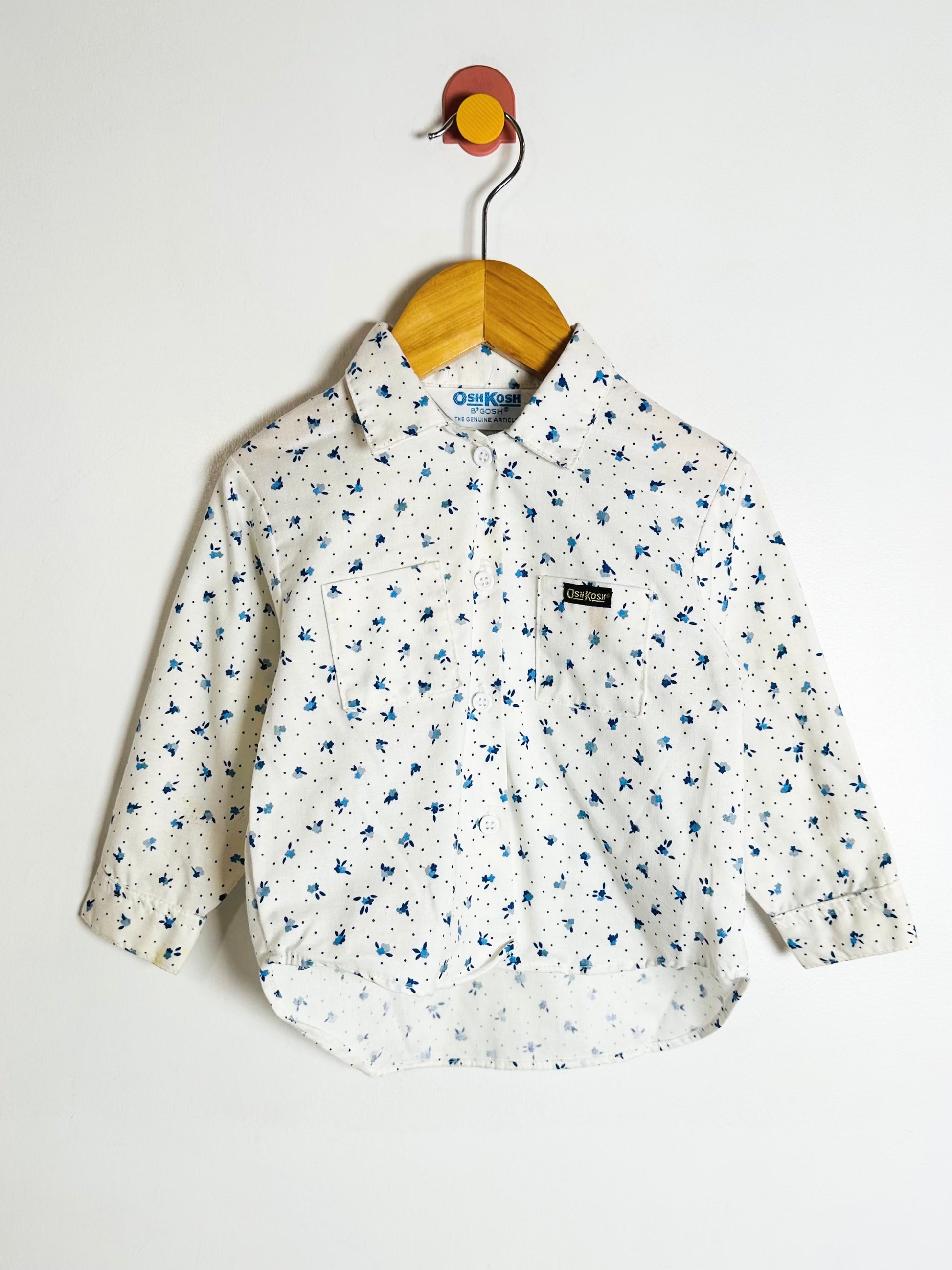 White floral-patterned shirt on a wooden hanger against a white background