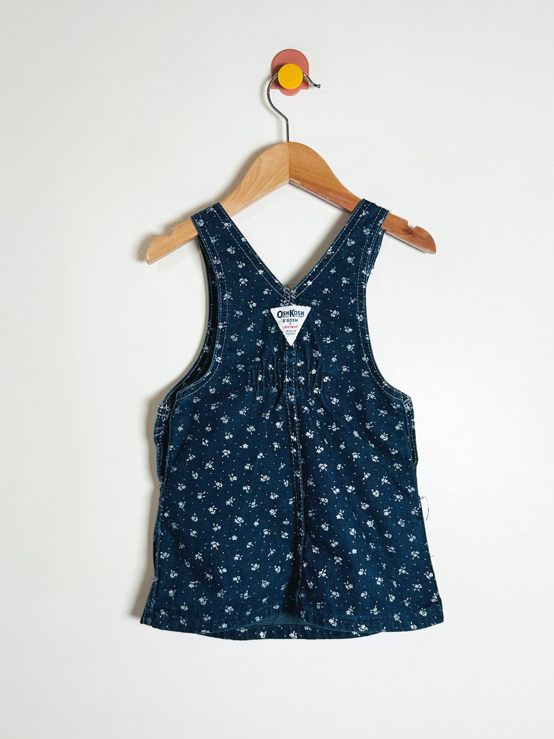 Blue floral-patterned romper on a wooden hanger against a white background