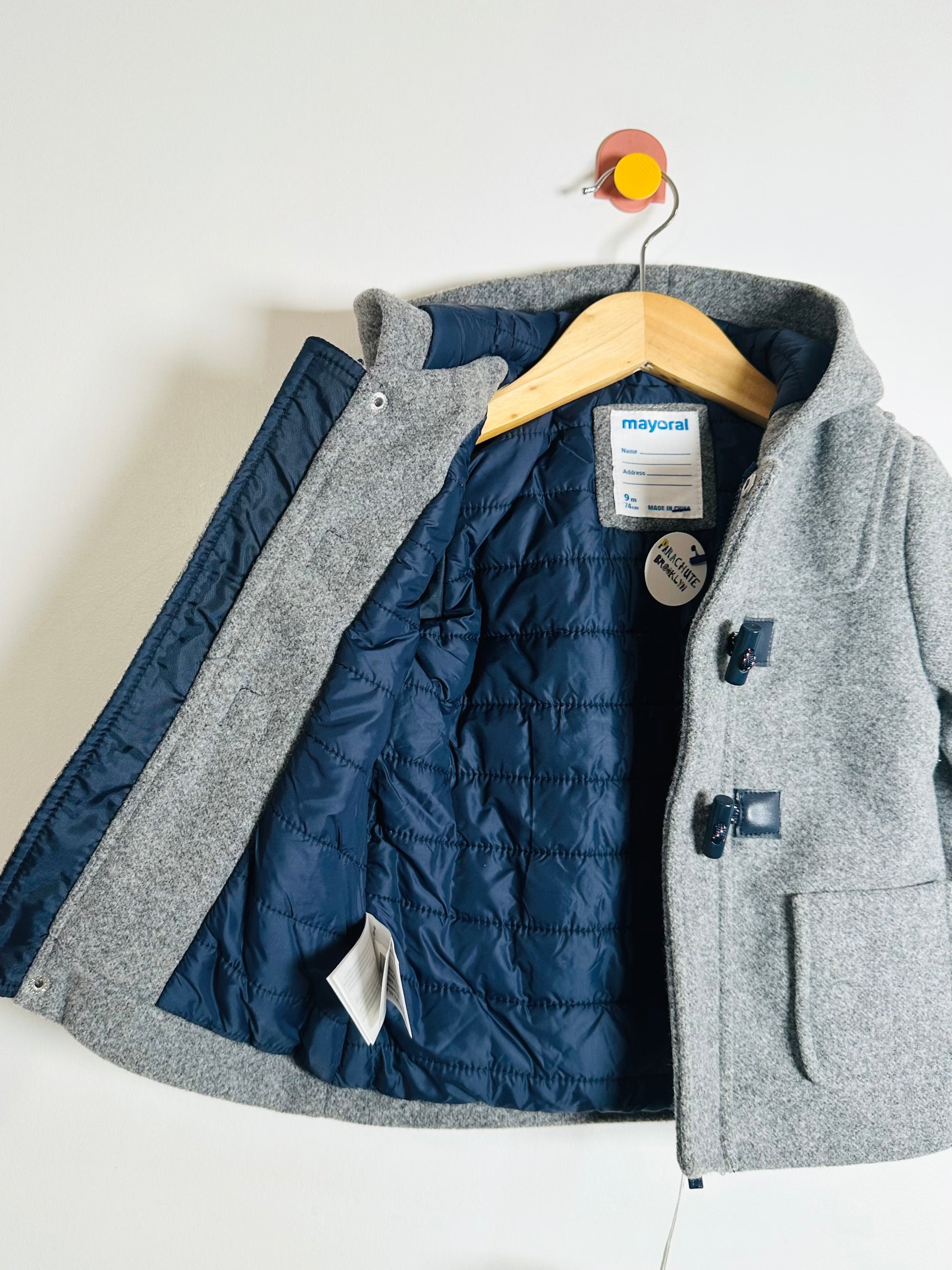 Gray jacket with a quilted navy lining on a hanger against a white background