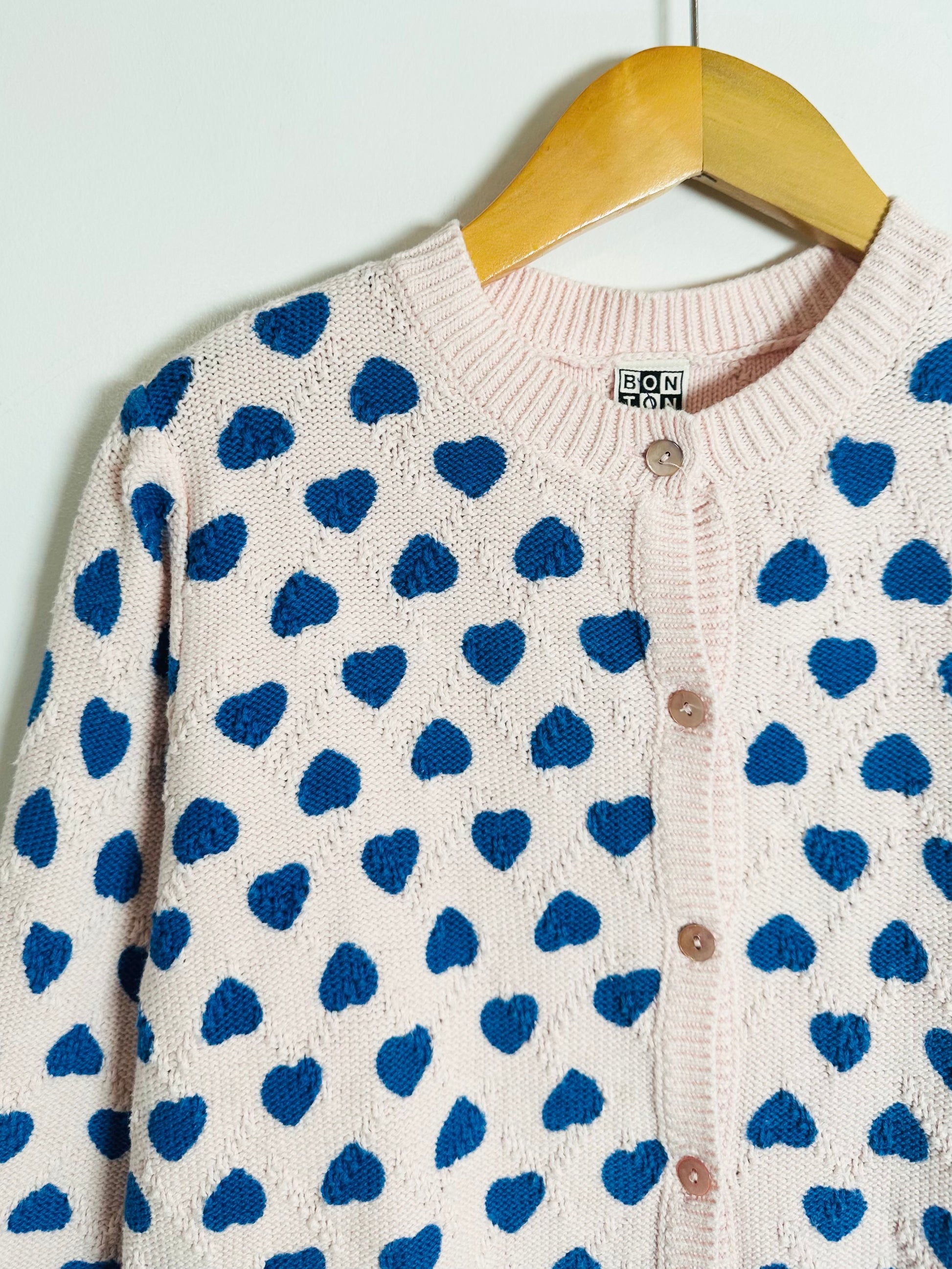 Cardigan with blue heart pattern on a hanger against a white background