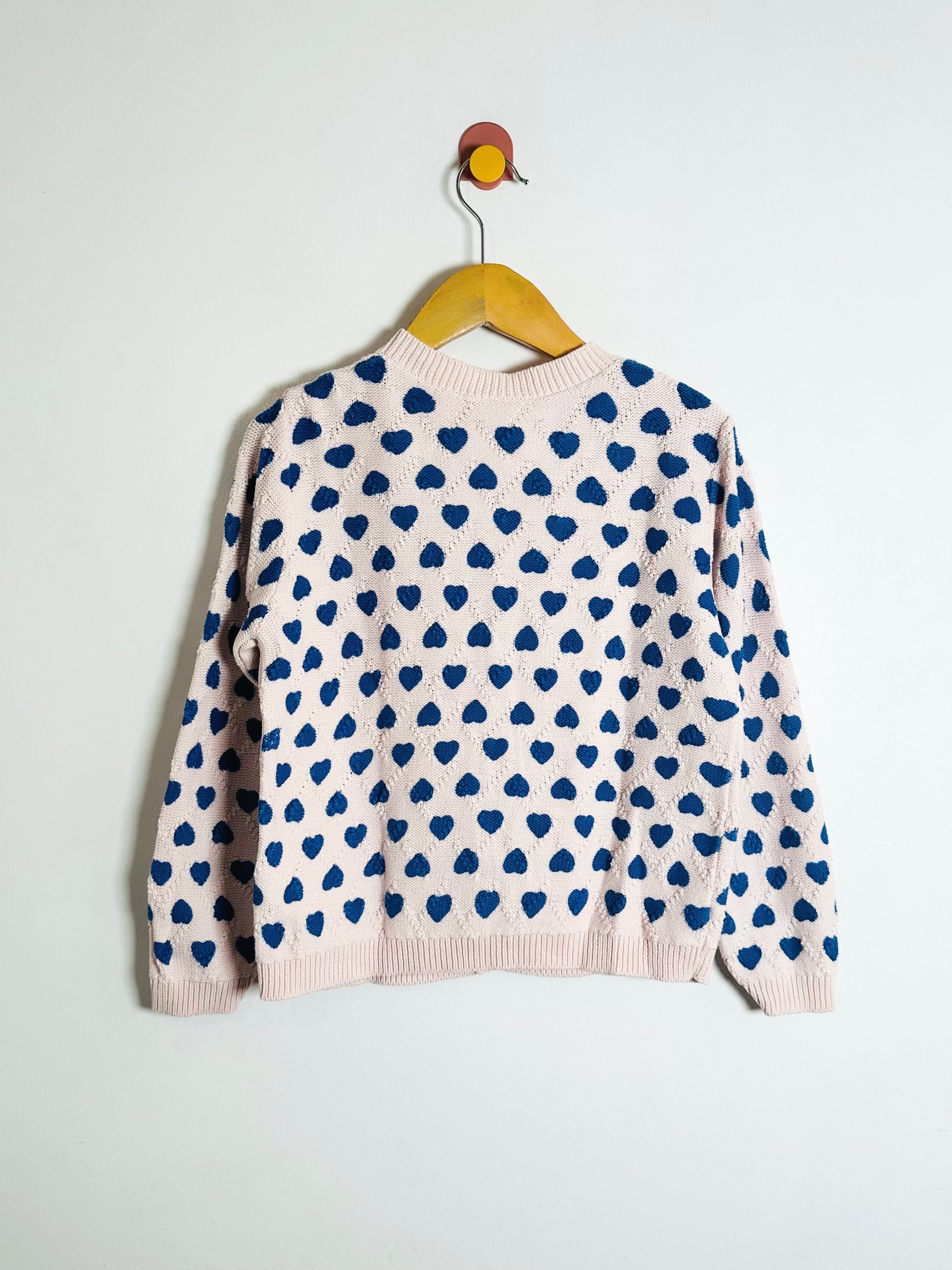 sweater with blue heart patterns on a hanger against a white background