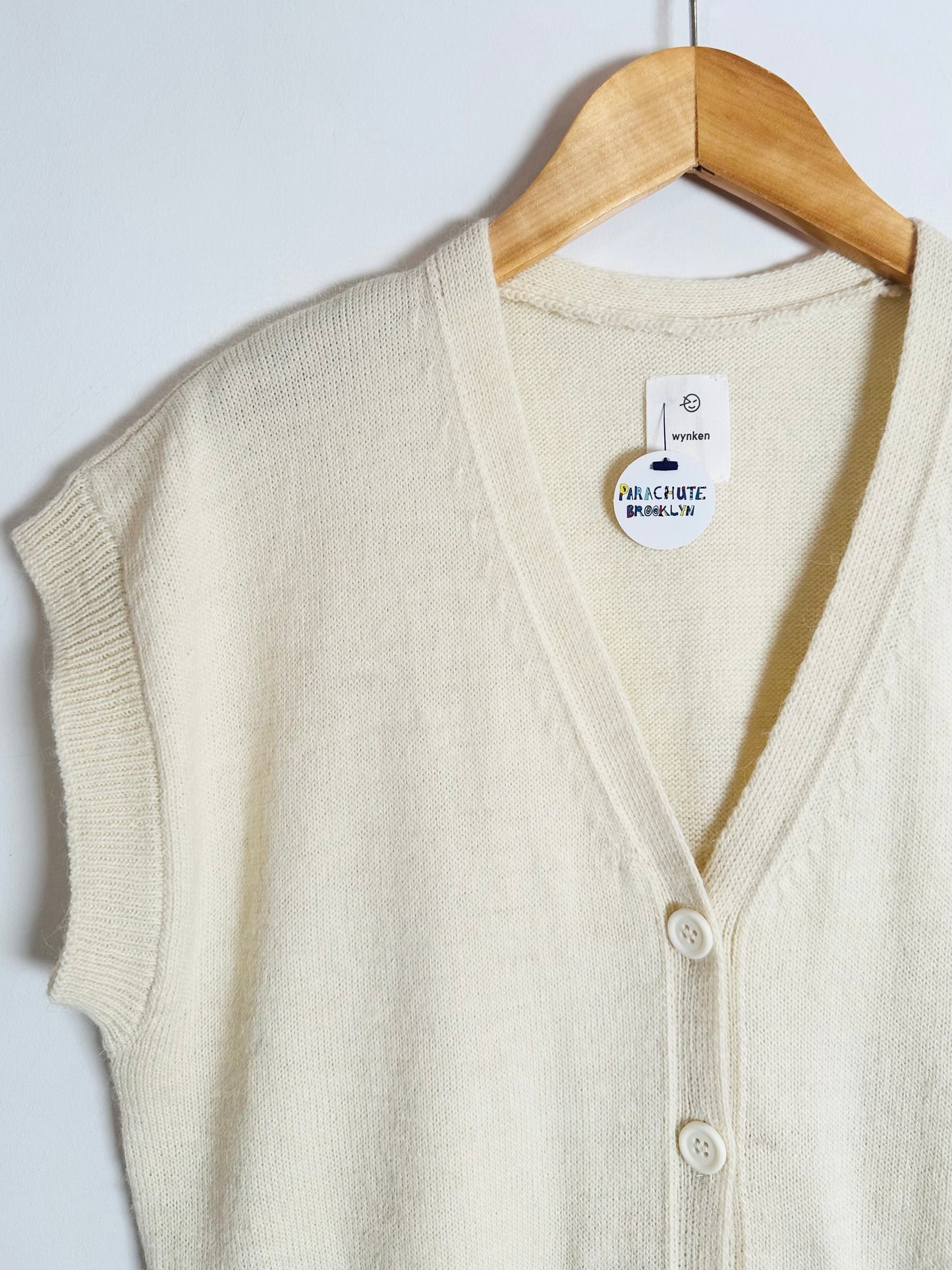 Beige cardigan on a wooden hanger with a visible brand tag against a white background