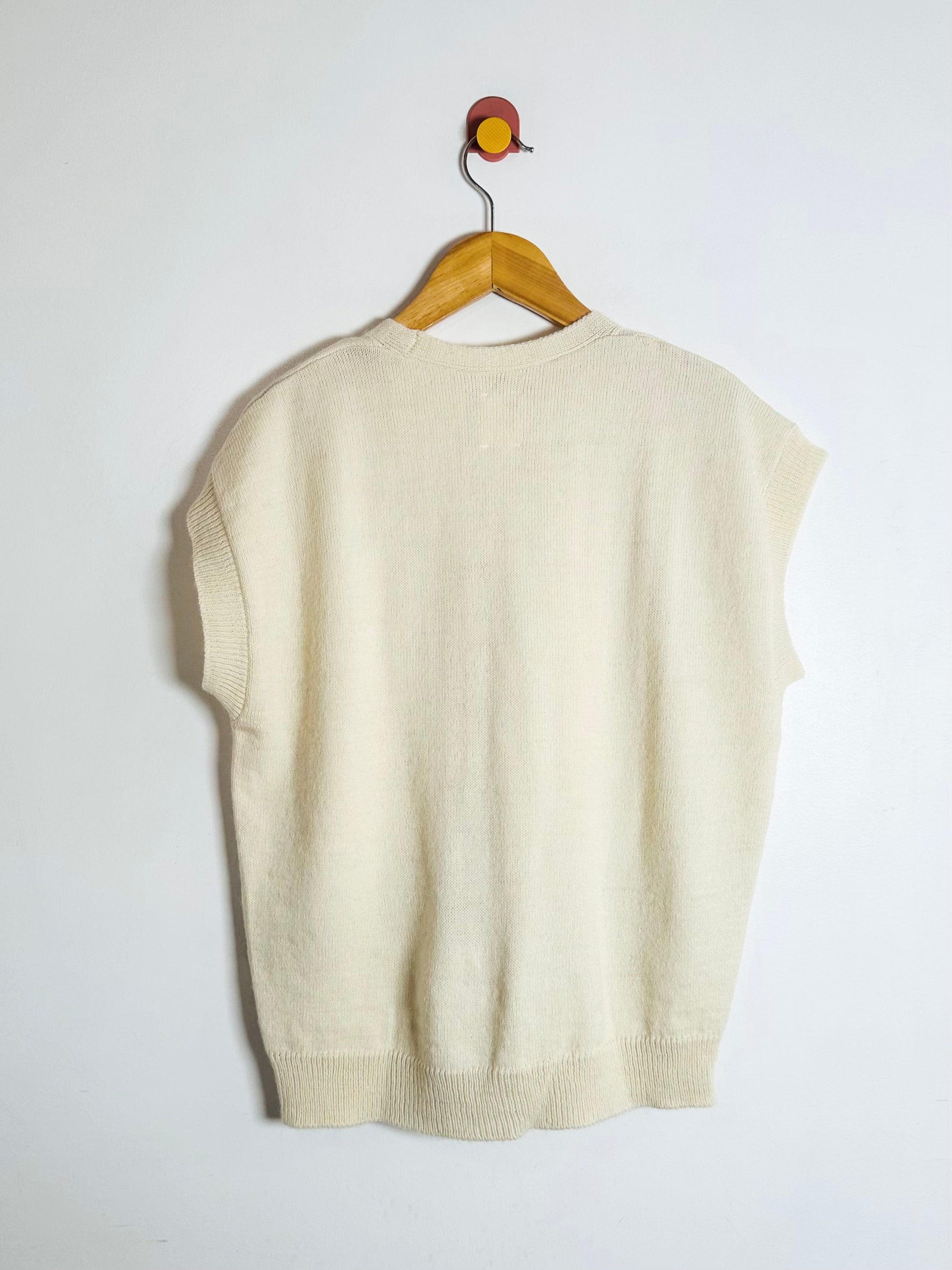 Beige sleeveless sweater on a wooden hanger against a white background