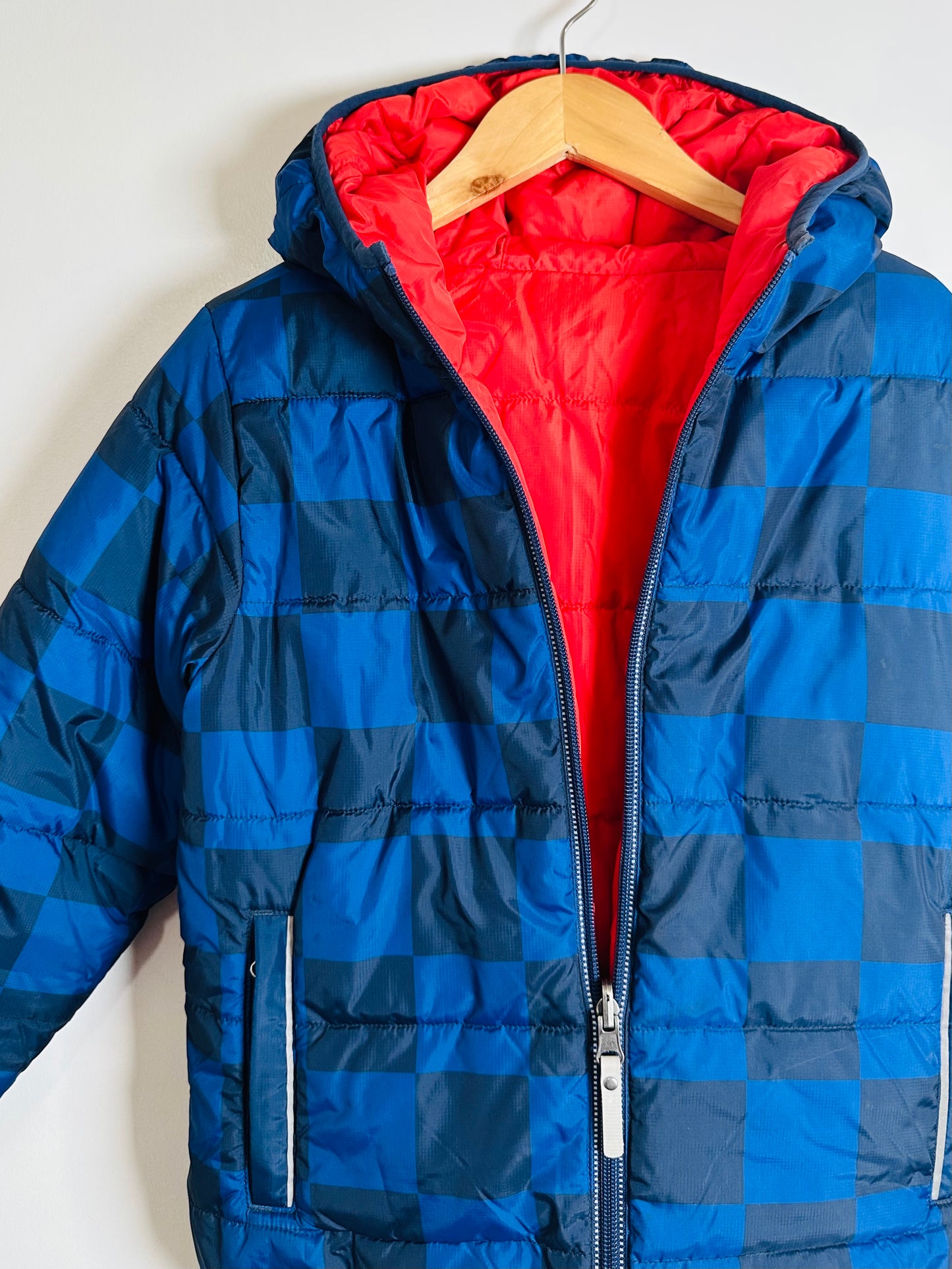 Blue checkered puffer jacket with red interior on a hanger against a white background