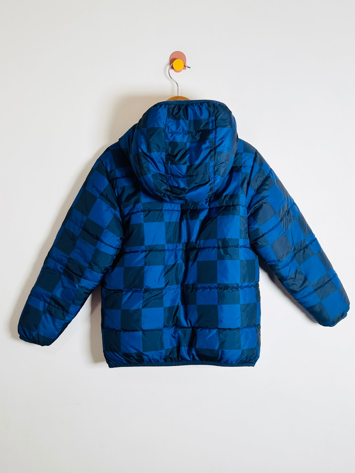 Blue checkered puffer jacket on a hanger against a white background