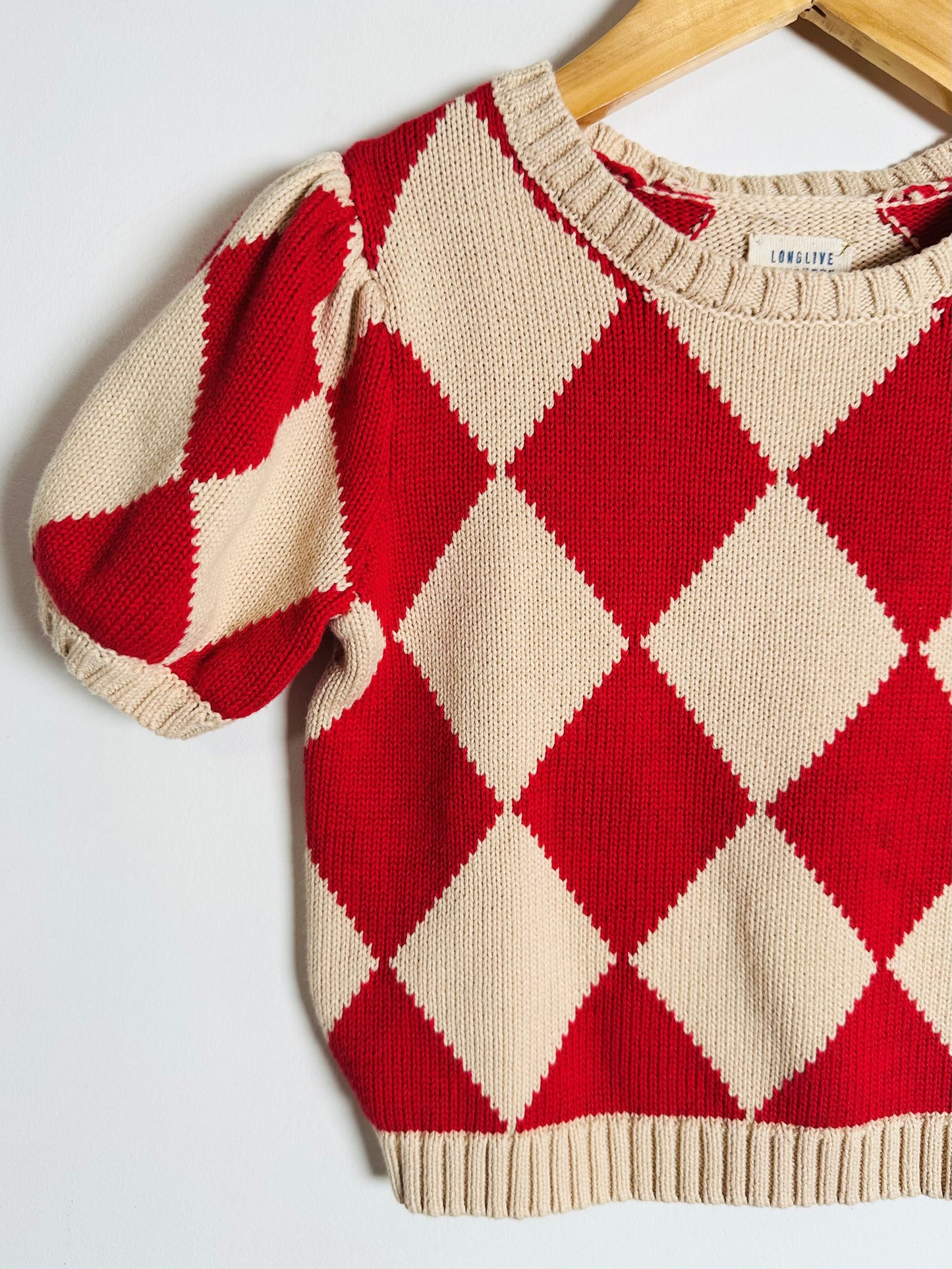 Red and beige diamond patterned sweater on a hanger against a white background