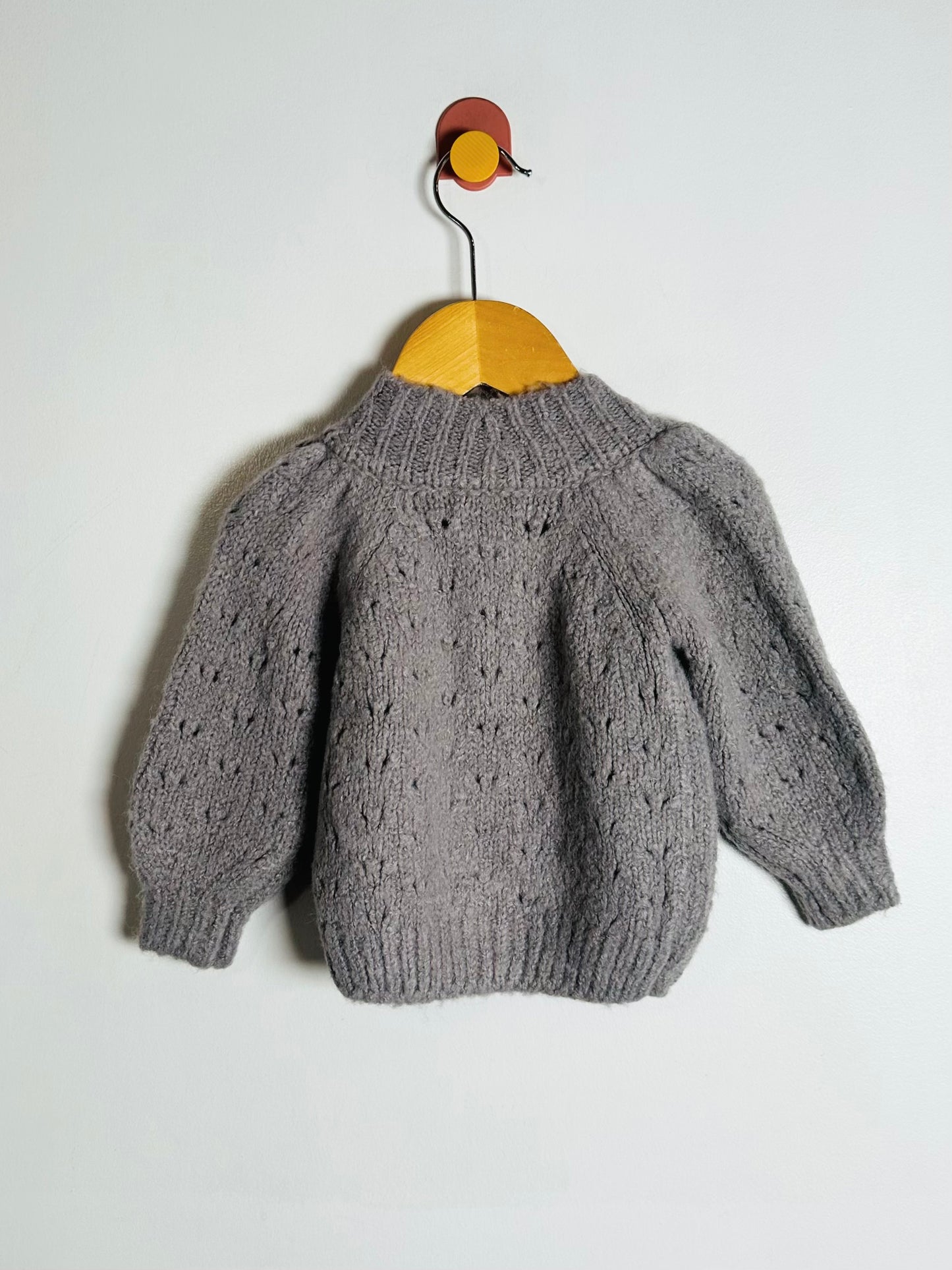 Gray knitted sweater on a wooden hanger against a white background