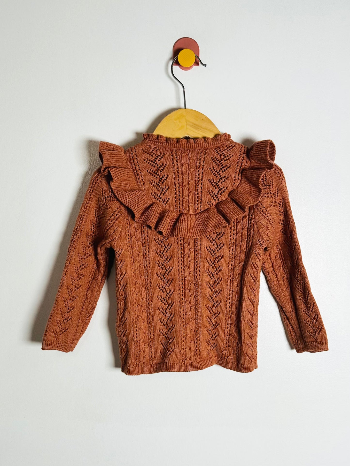 Brown knitted sweater with ruffled details on a white background